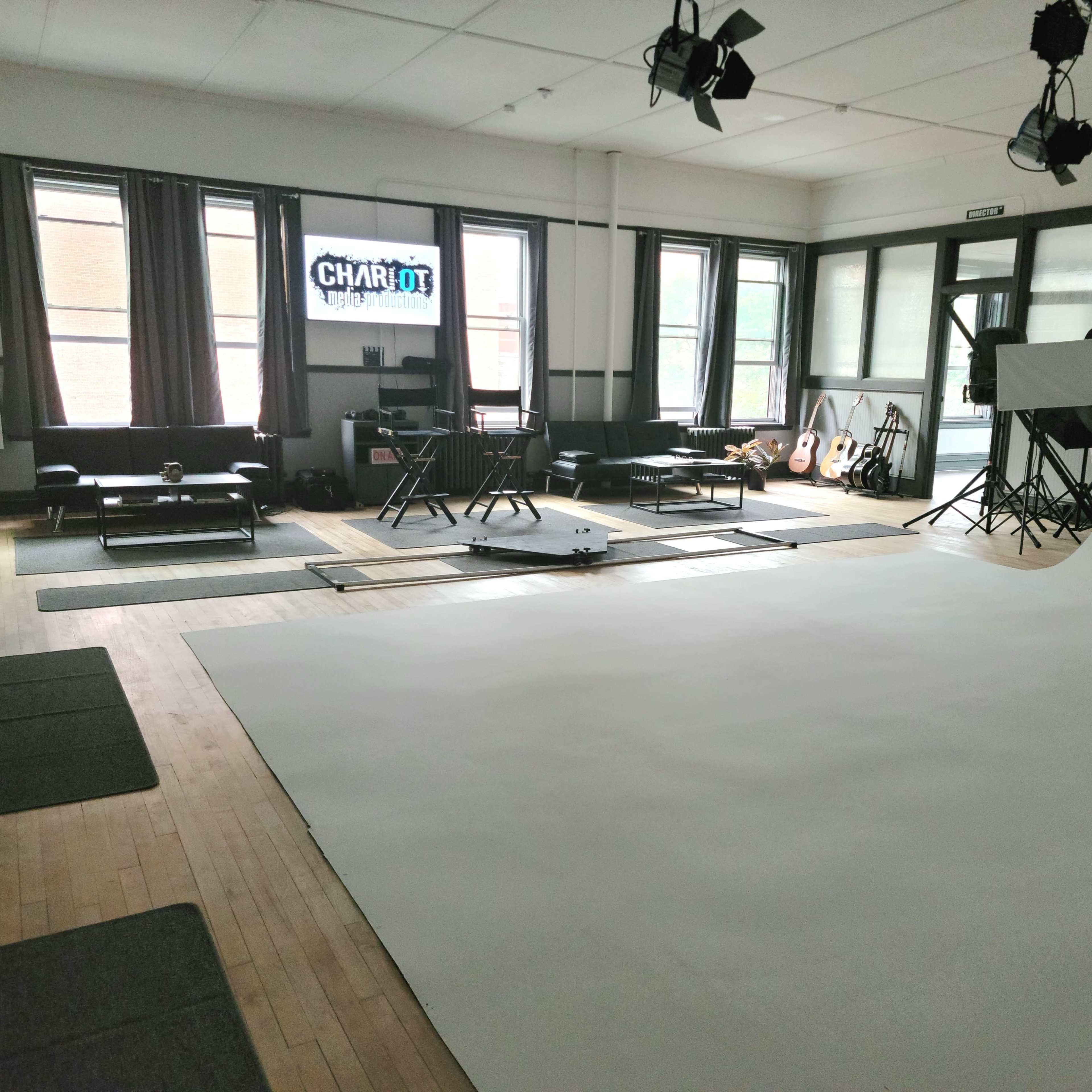 A spacious photography studio featuring a white backdrop, comfortable seating areas, and various photographic equipment.