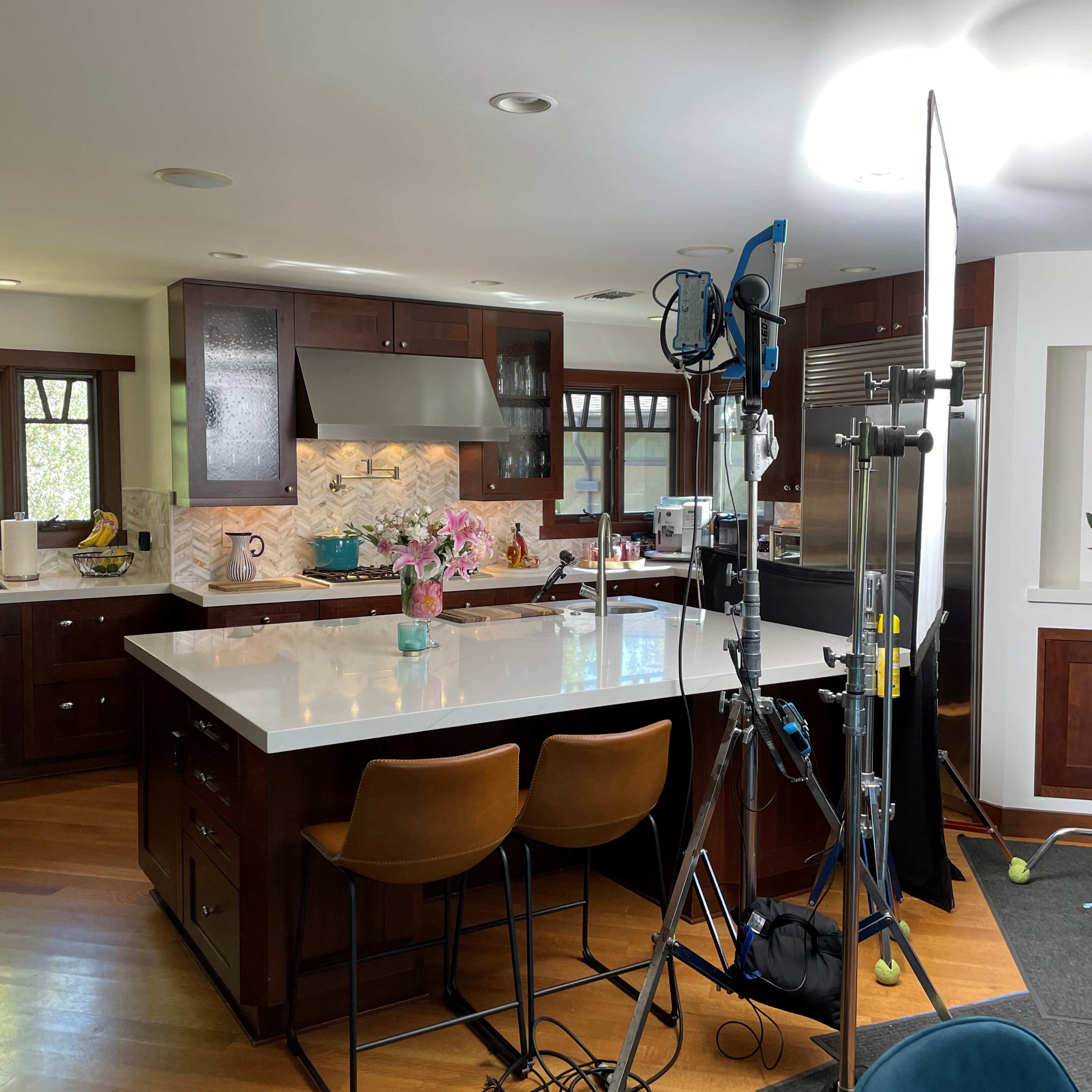 A modern kitchen with dark wood cabinets, a large white island, and a professional lighting setup for filming.