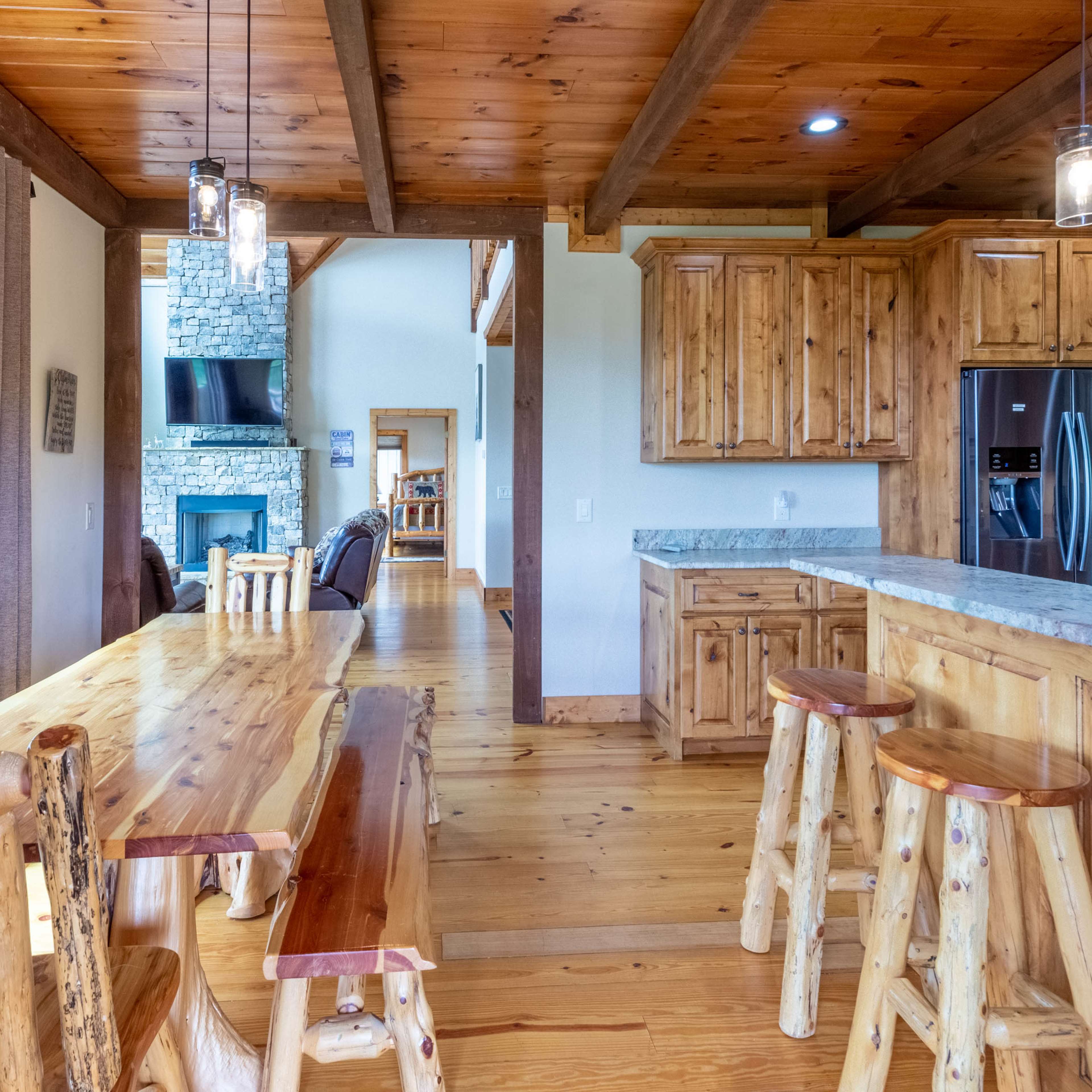A rustic kitchen and dining area featuring wooden furnishings, a stone fireplace, and a light-filled open layout.