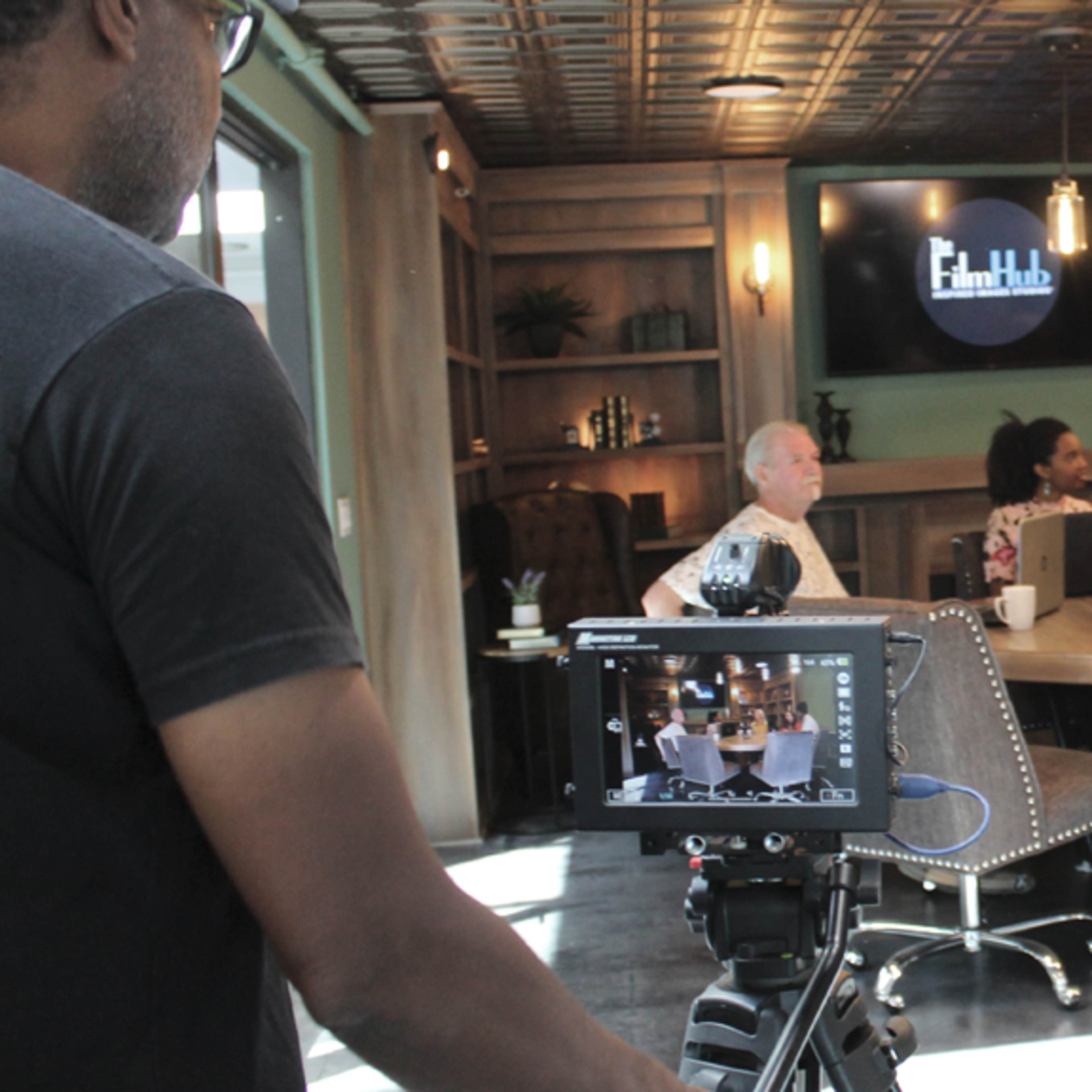 A group of people is seated at a table in a modern meeting space equipped with cameras and recording equipment.