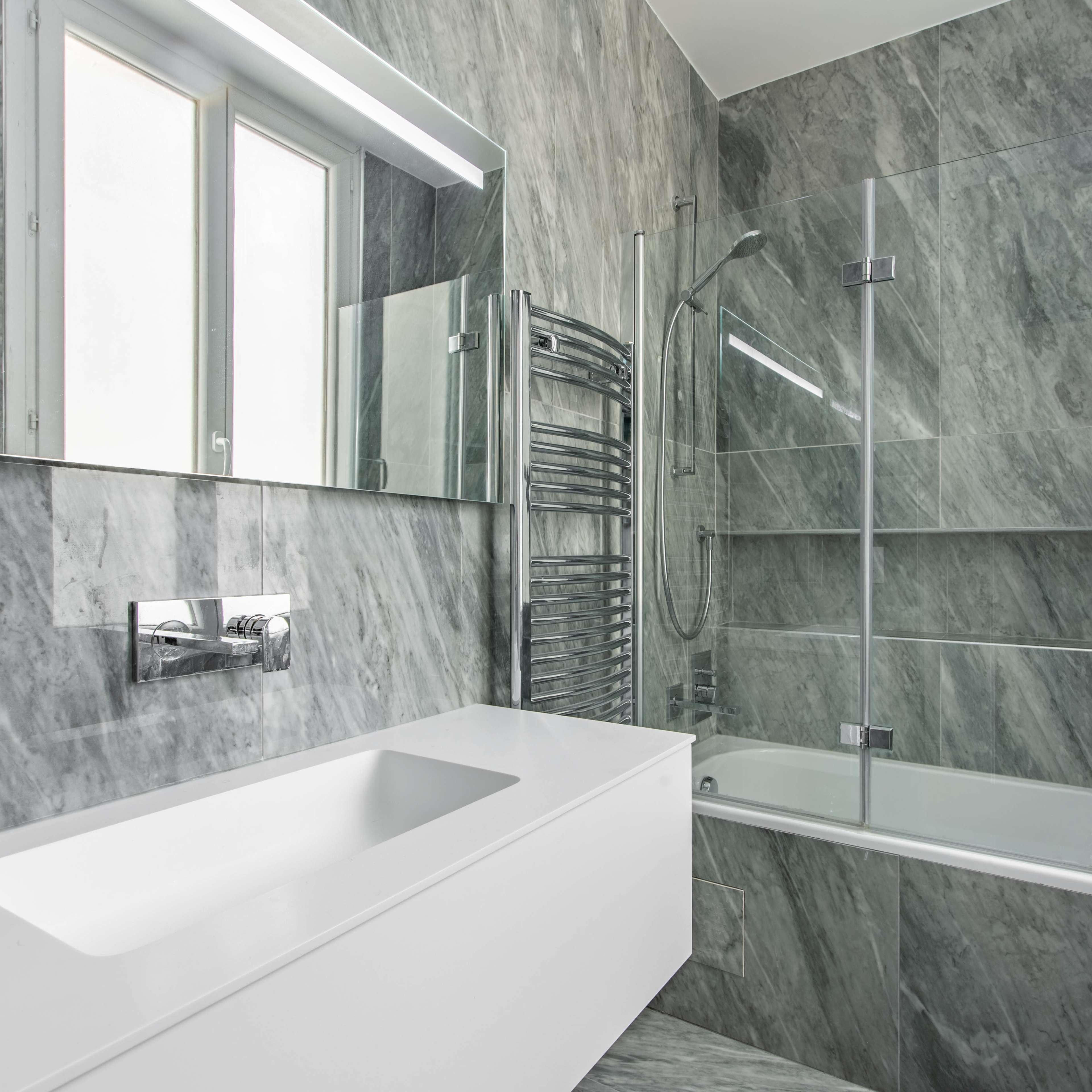 A modern bathroom featuring a freestanding bathtub, a glass shower enclosure, marble walls, and sleek fixtures.