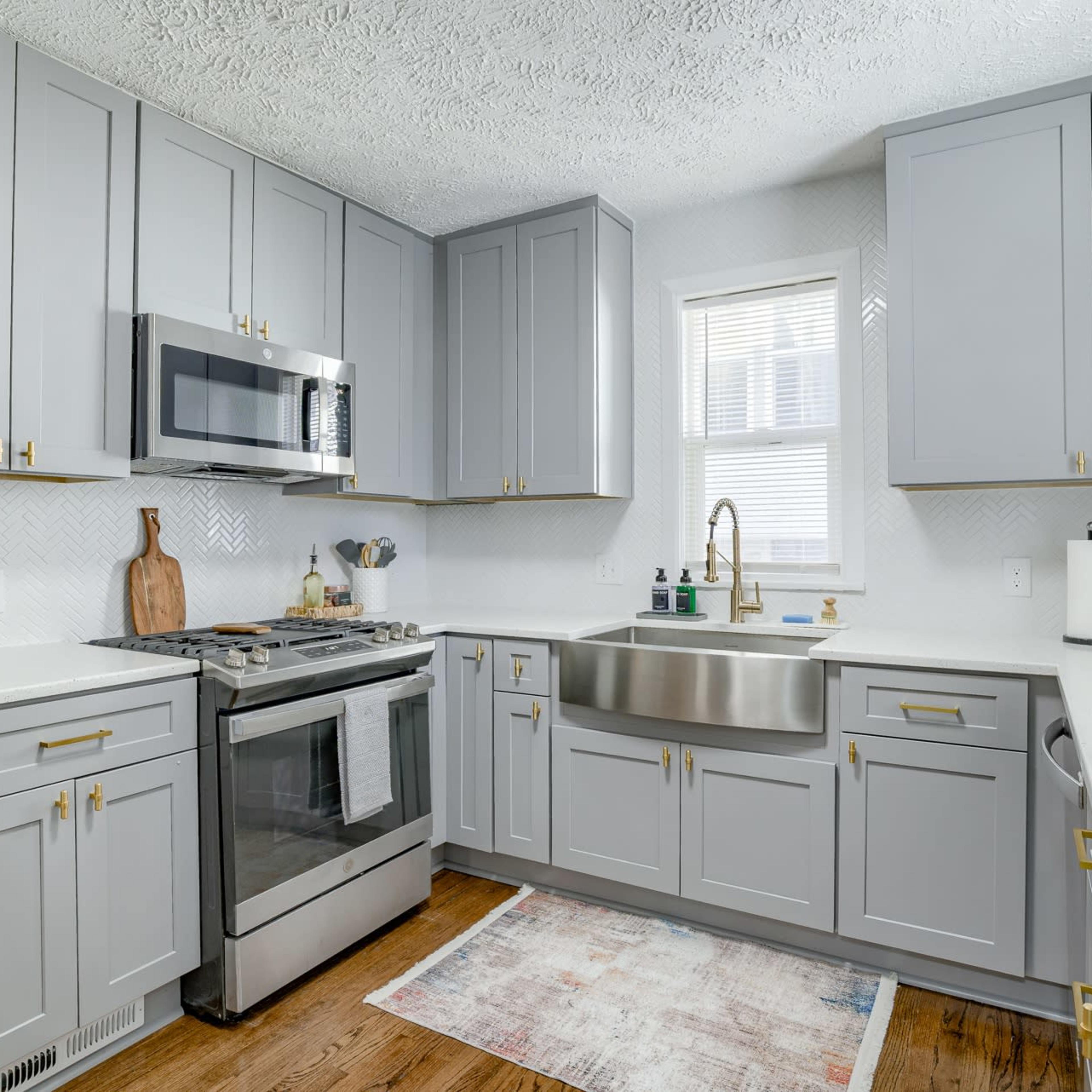 A modern kitchen features gray cabinets, a stainless steel gas stove, a farmhouse sink, and a large window that lets in natural light.