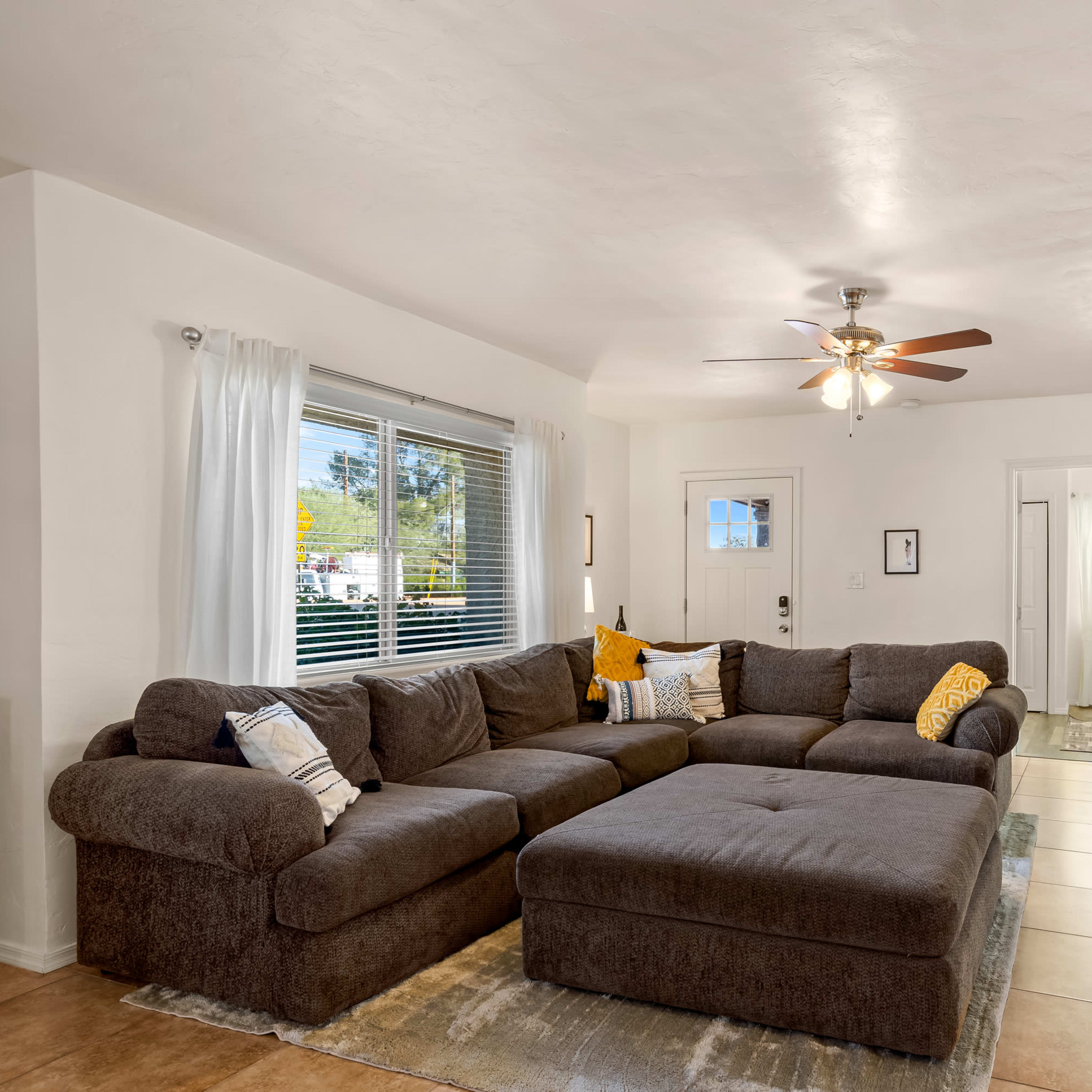 The living room features a large brown sectional sofa, a ceiling fan, and a TV mounted on the wall.