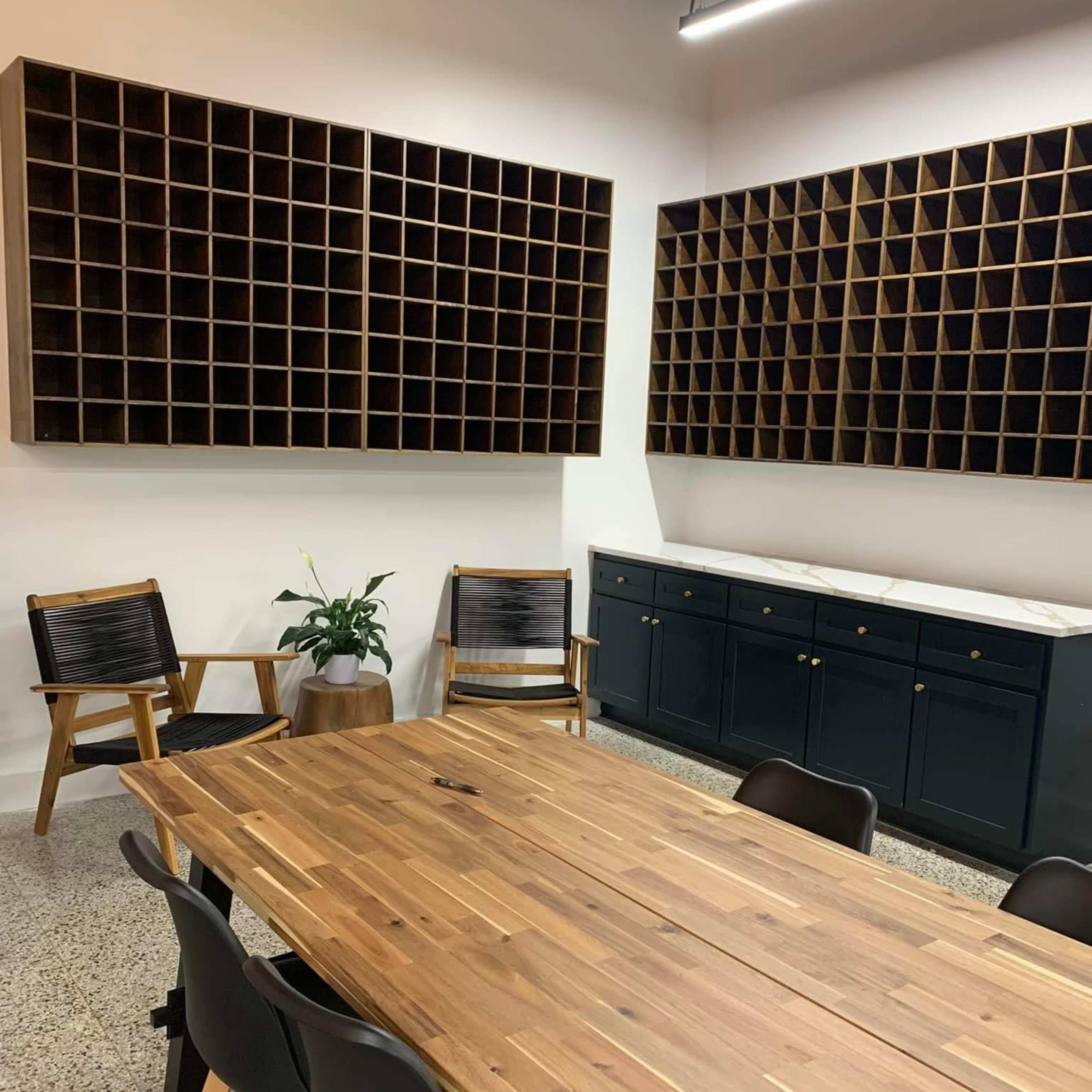 A conference room features a large wooden table surrounded by chairs, with wooden cubby shelves and a cabinet along the walls.
