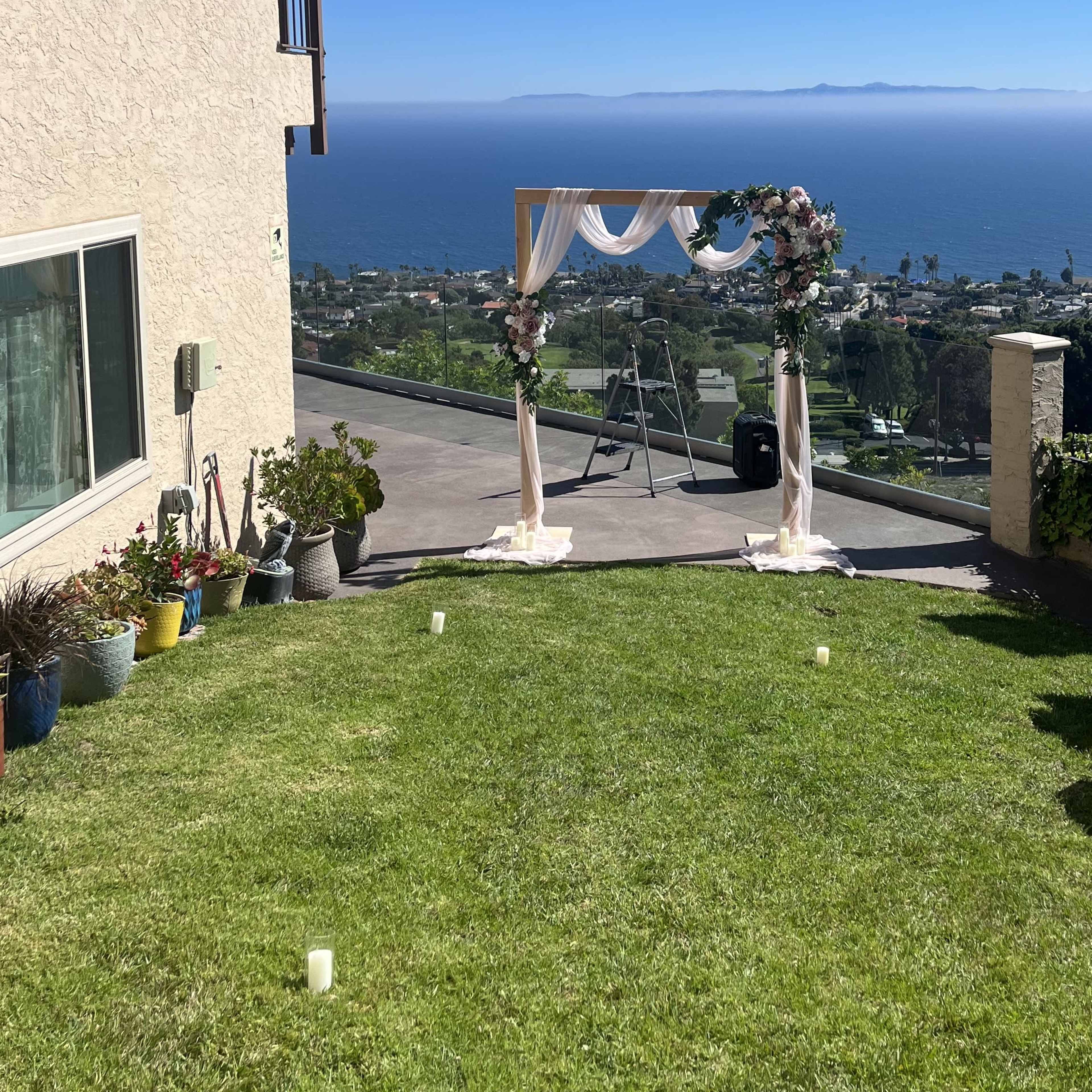 A floral arch is set up on a grassy area overlooking the ocean and coastline in the background.