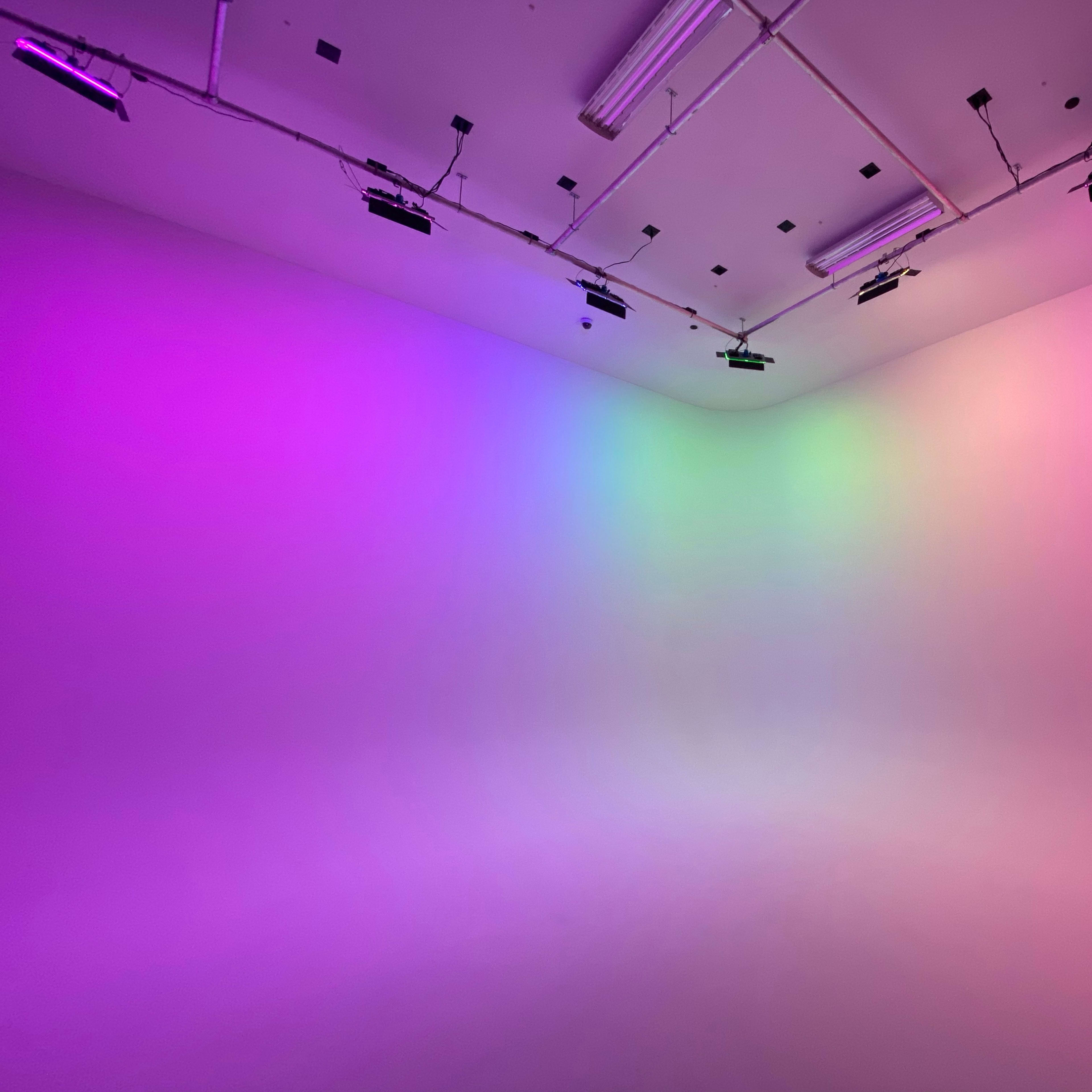 A studio space features walls illuminated with gradient purple and green lighting.