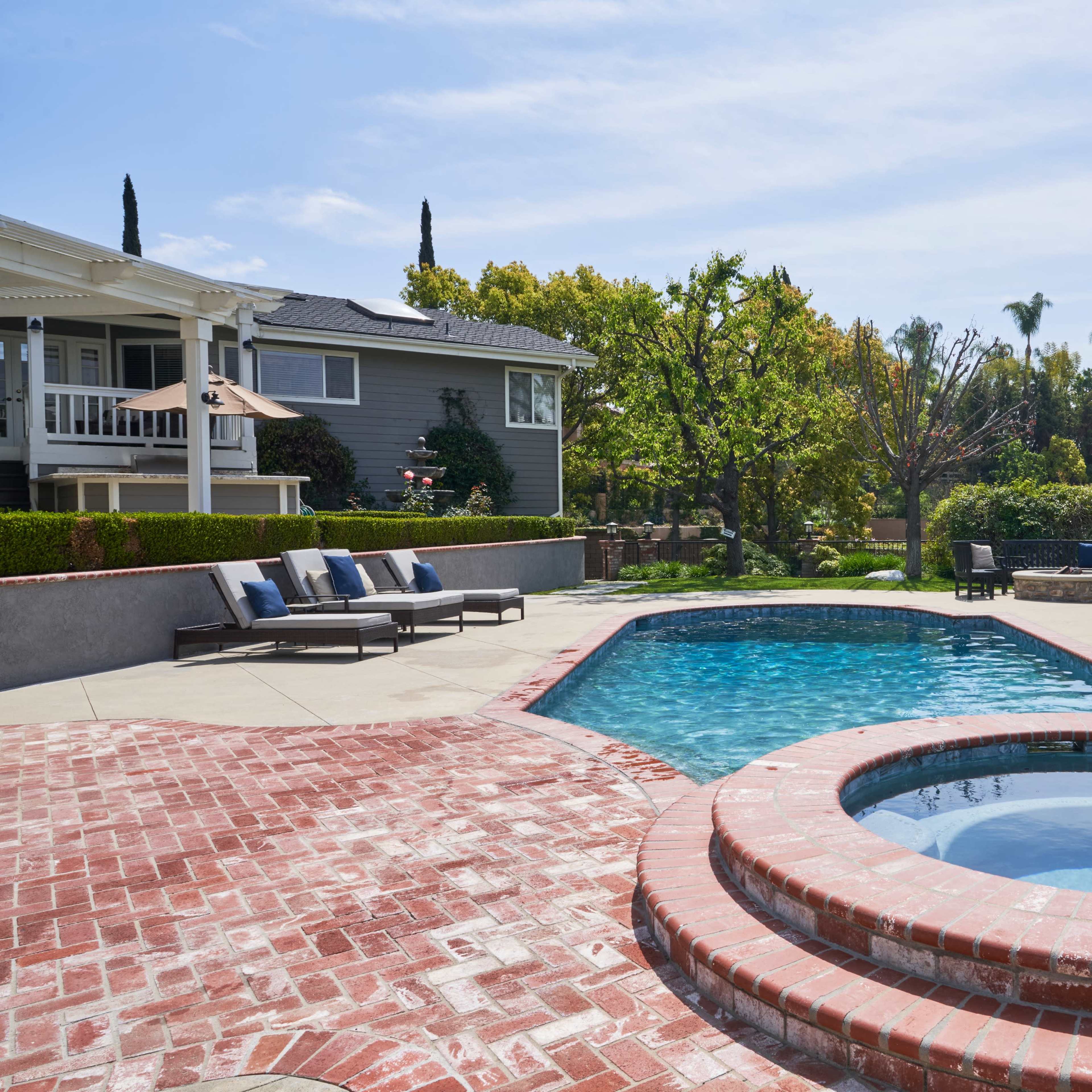 A backyard with a swimming pool and a spa, surrounded by landscaped greenery and residential buildings.