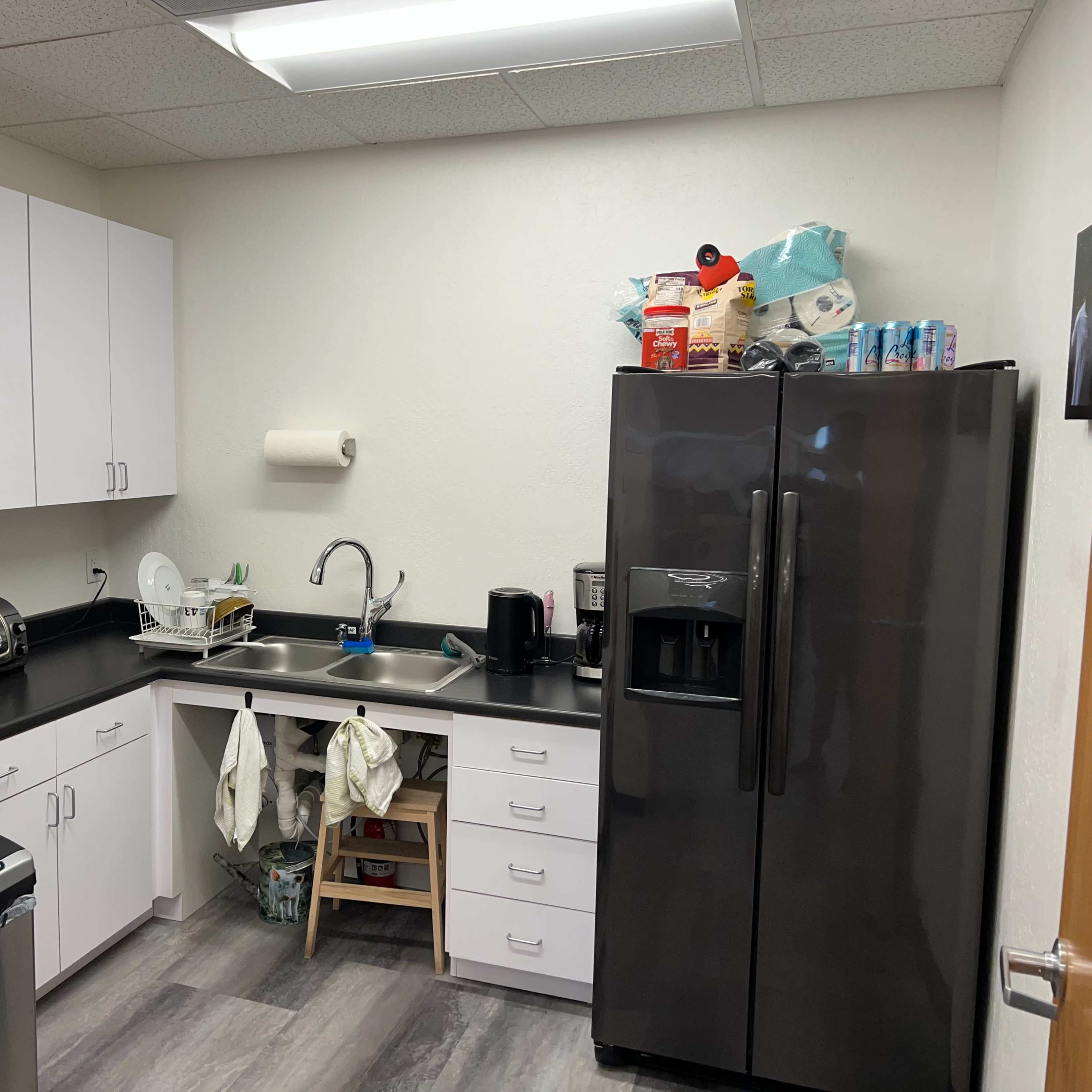 A small kitchen is equipped with white cabinets, a black refrigerator, a sink, and various kitchen appliances and items on the counters.