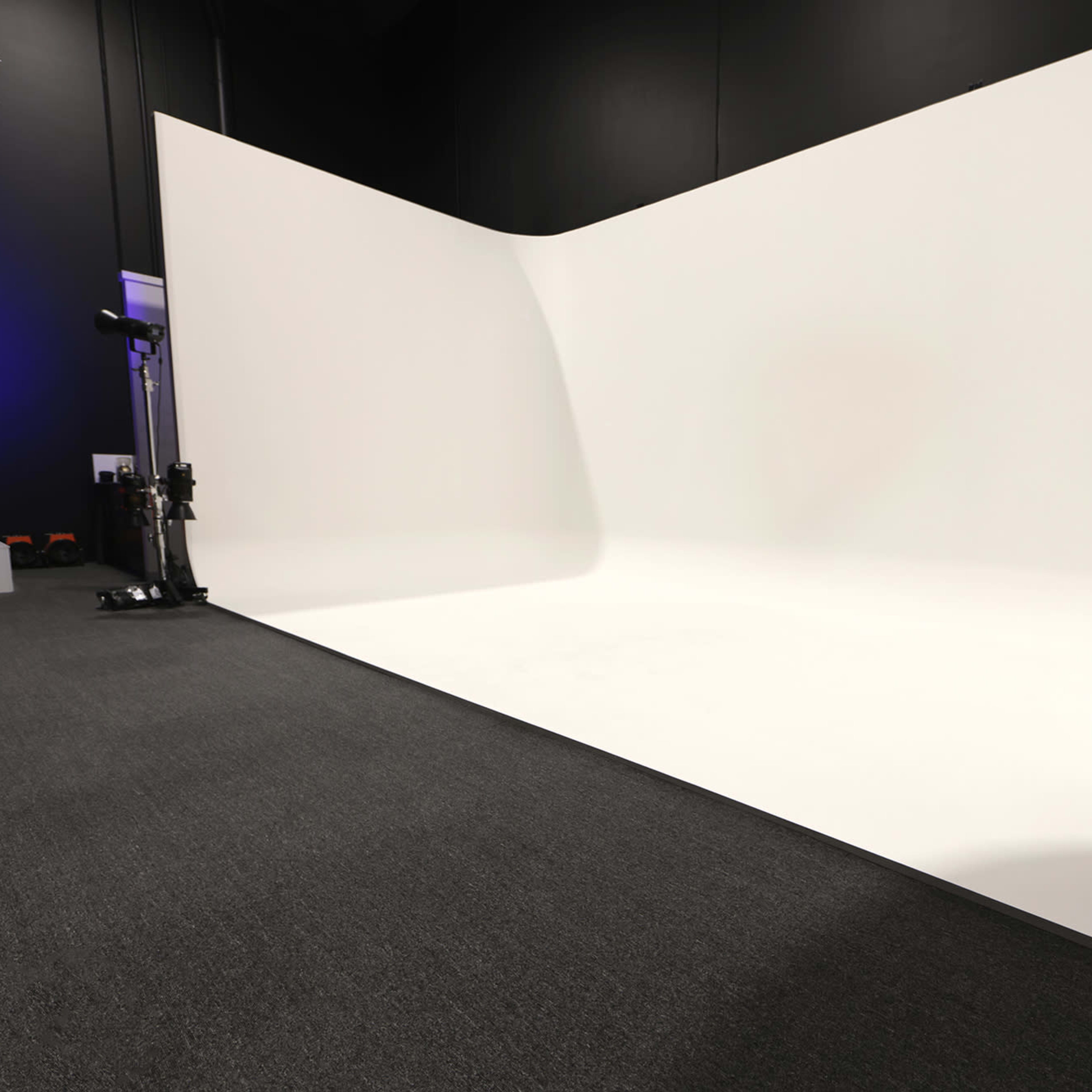A spacious photography studio with a seamless white backdrop and dark gray carpet.
