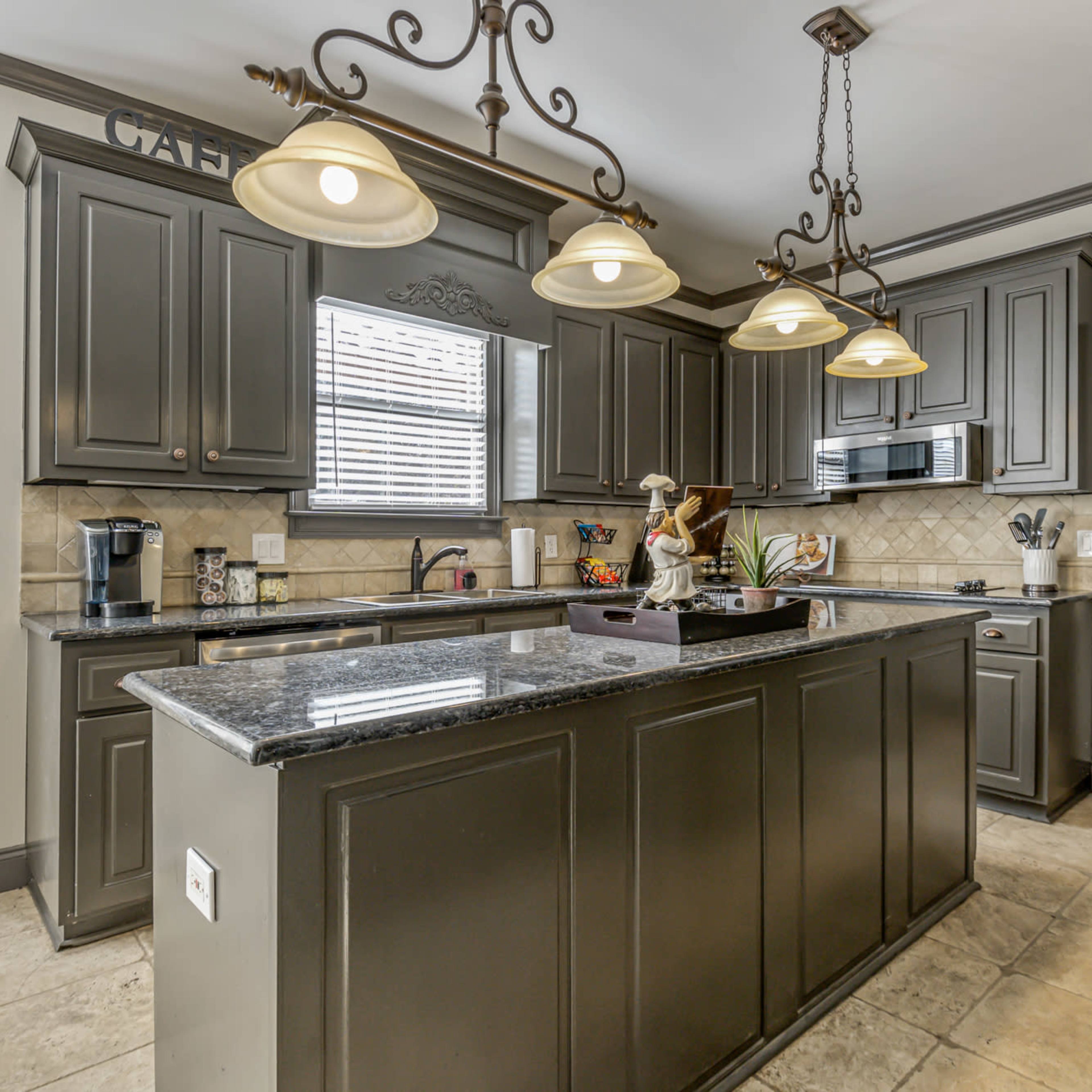 A modern kitchen with dark cabinetry, a granite countertop, and pendant lighting over an island.