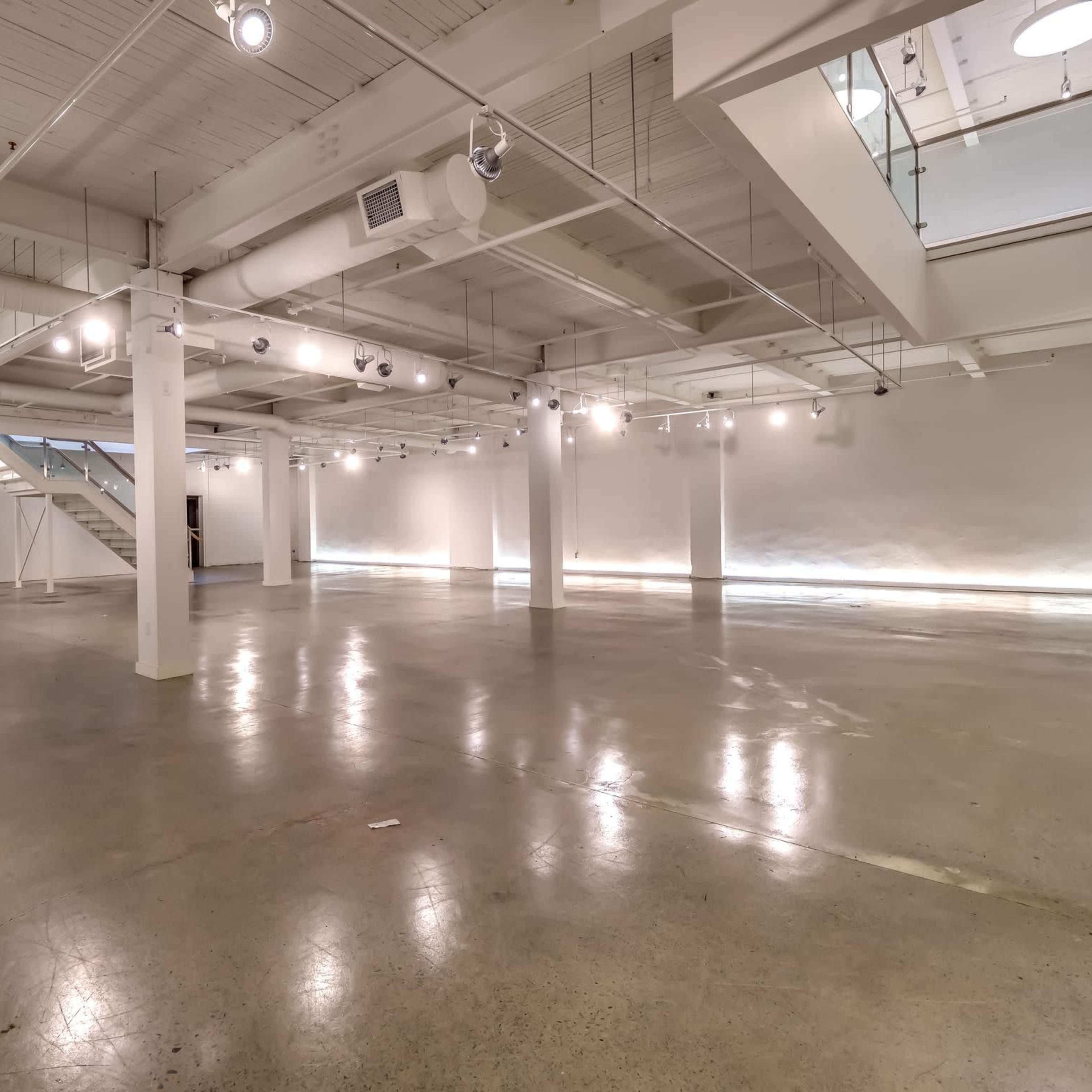 A spacious, minimally furnished interior with concrete flooring and white walls, illuminated by overhead lights.