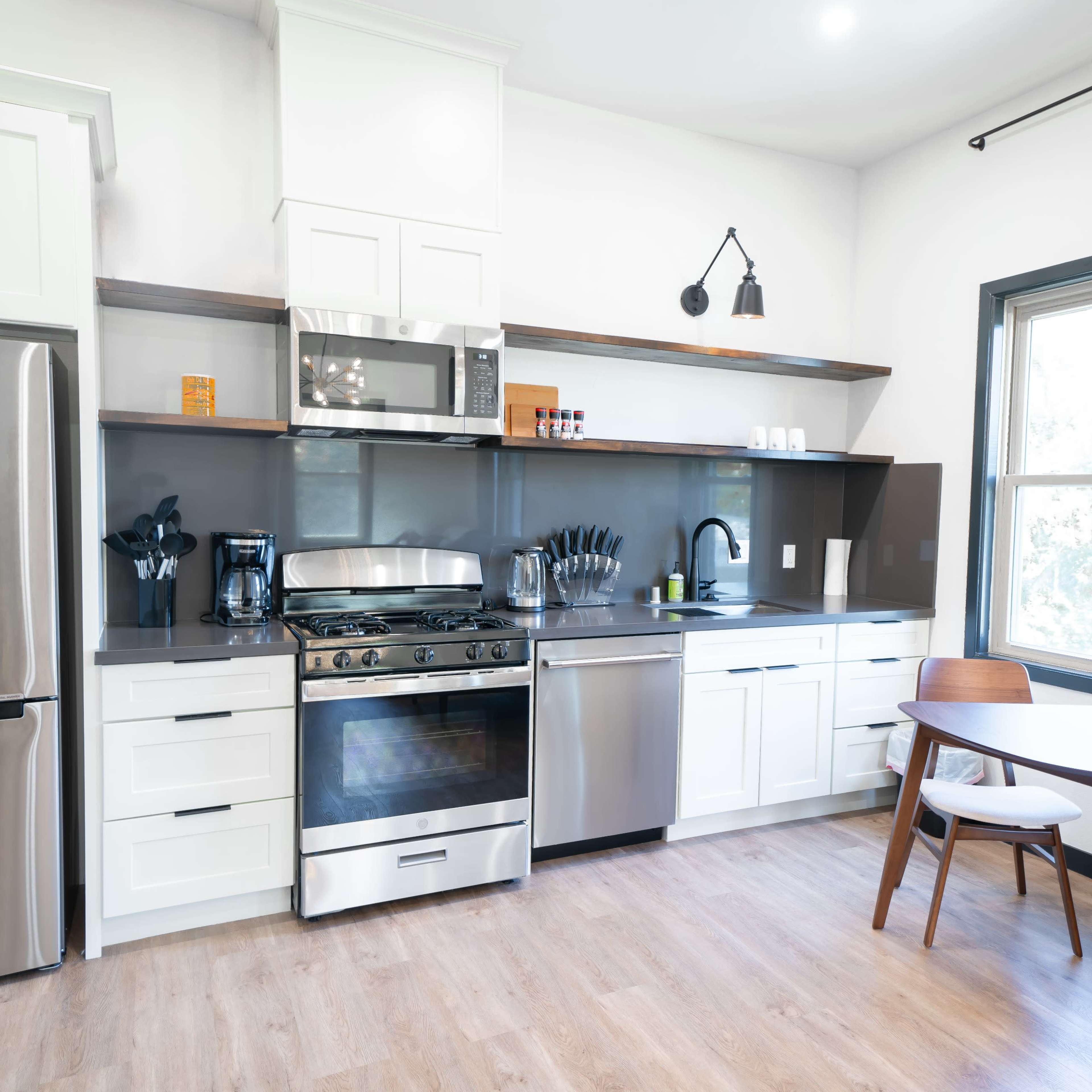 A modern kitchen with stainless steel appliances, white cabinetry, and a circular wooden dining table with two chairs.