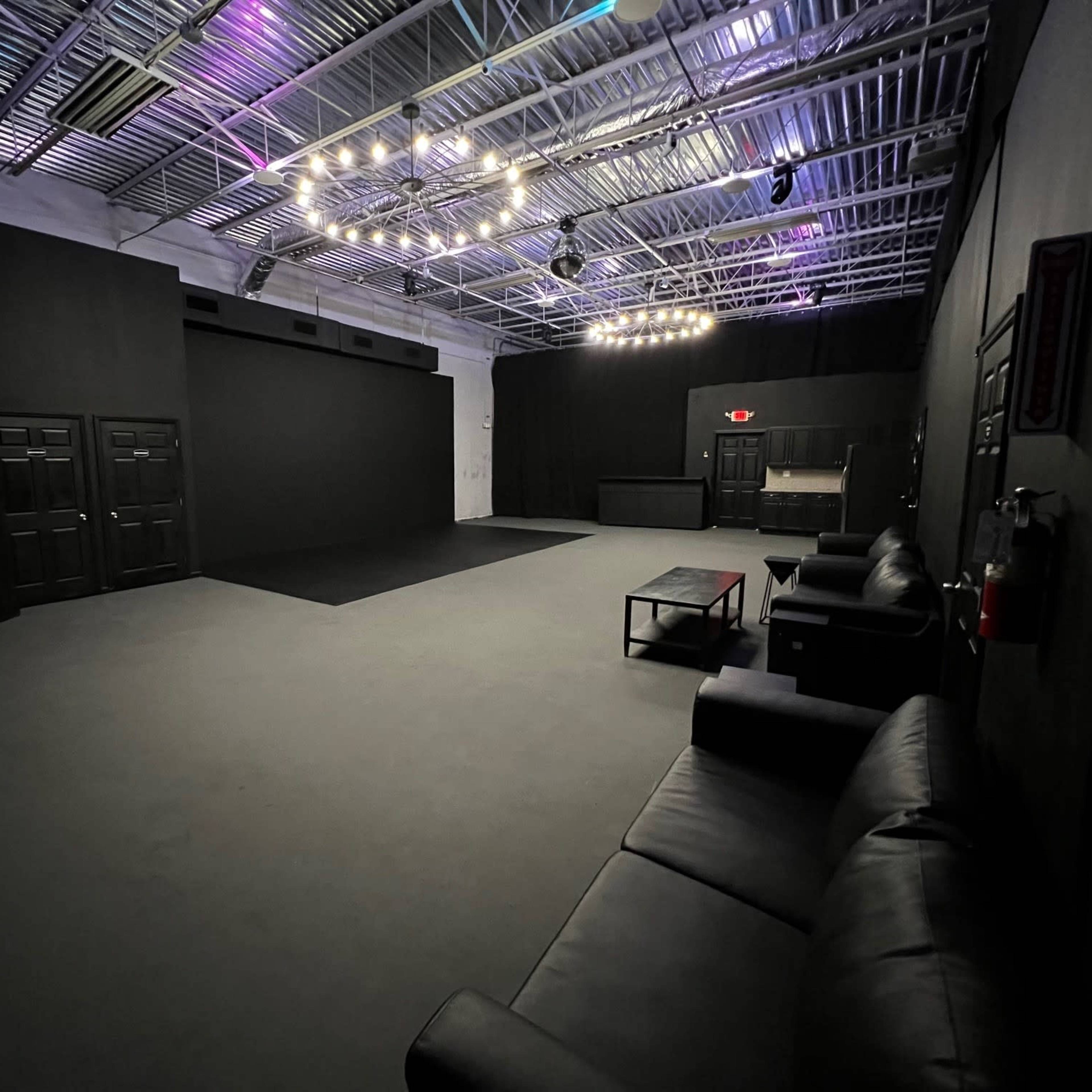 An empty black-walled studio space with a seating area, dim lighting, and a polished floor.