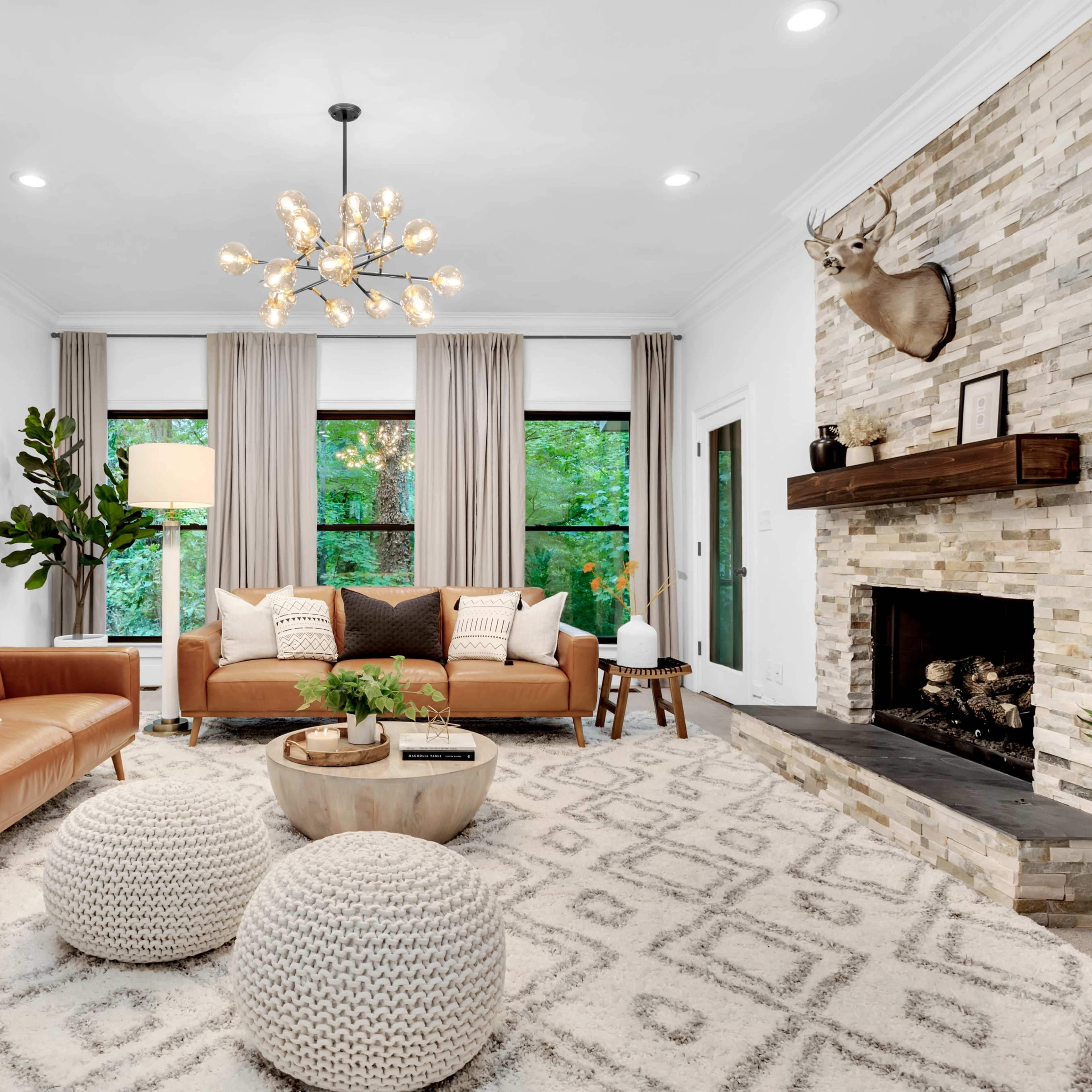 A cozy living room features a stone fireplace, modern furniture, and large windows that overlook greenery.