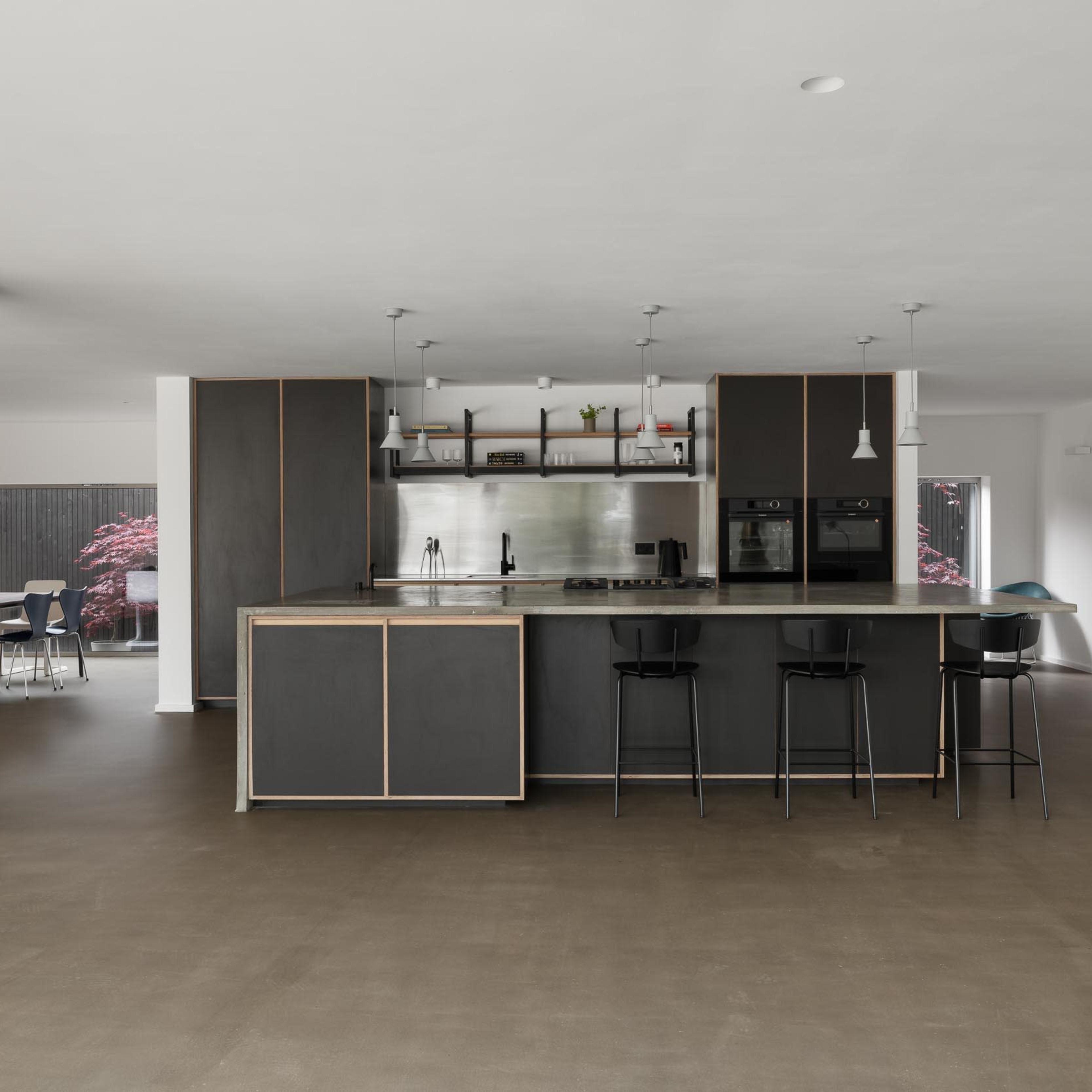 A modern kitchen features a central island with bar stools, stainless steel appliances, and minimalist cabinetry in an open-concept layout.