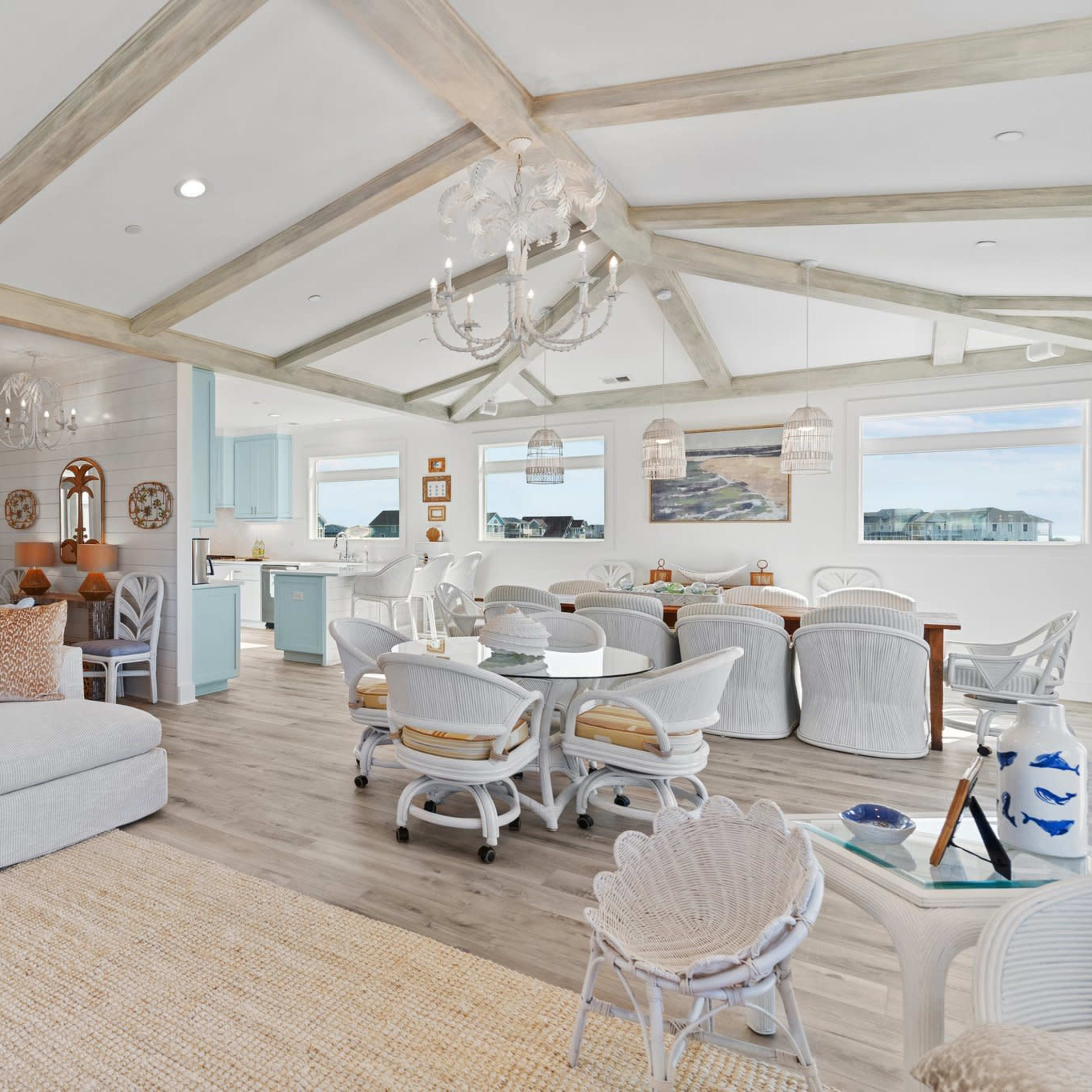 A bright, open living and dining area featuring a light-colored sectional sofa, a dining table surrounded by white chairs, and large windows that allow natural light to fill the space.