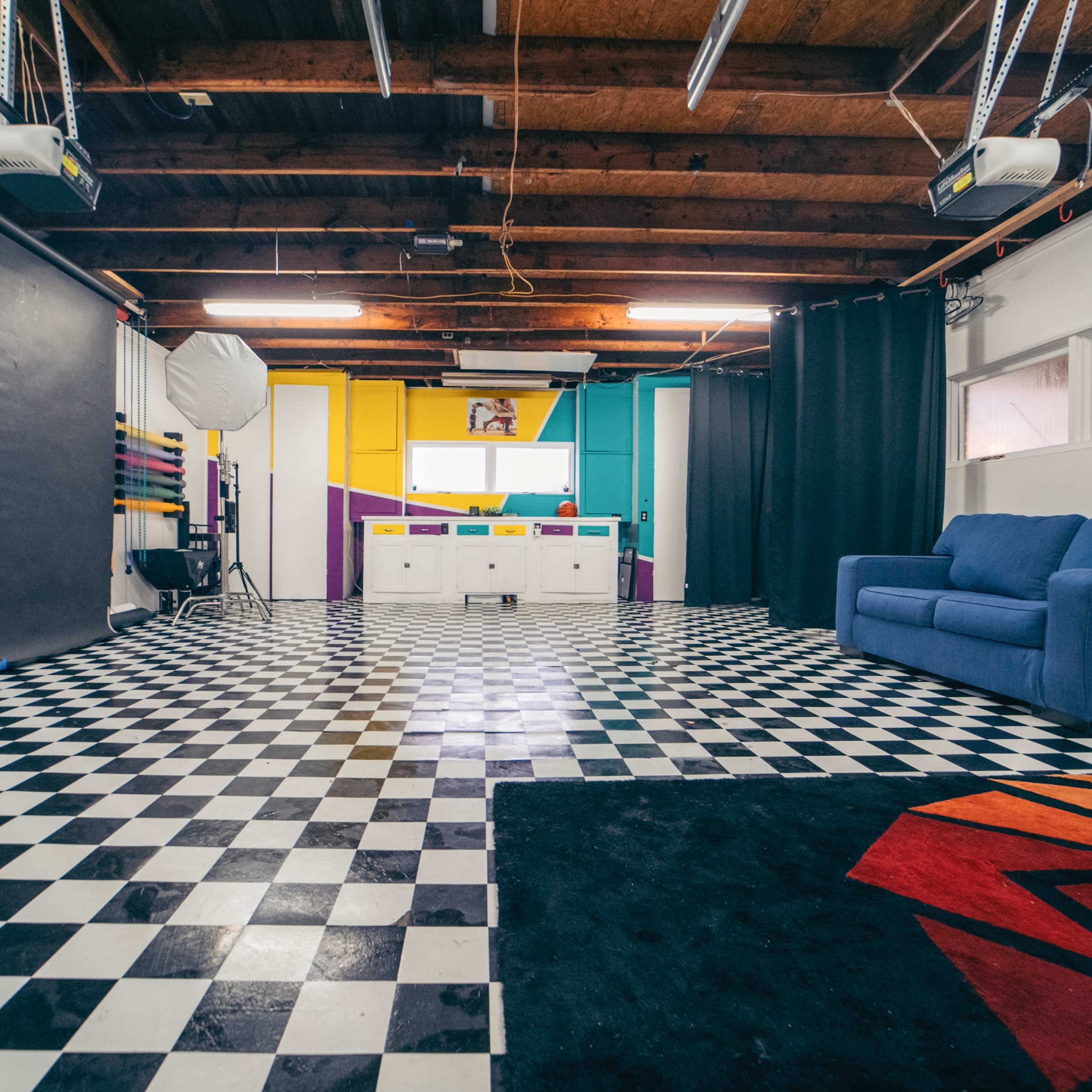 A spacious studio featuring a checkered floor, a blue couch, and colorful walls with various lighting equipment.