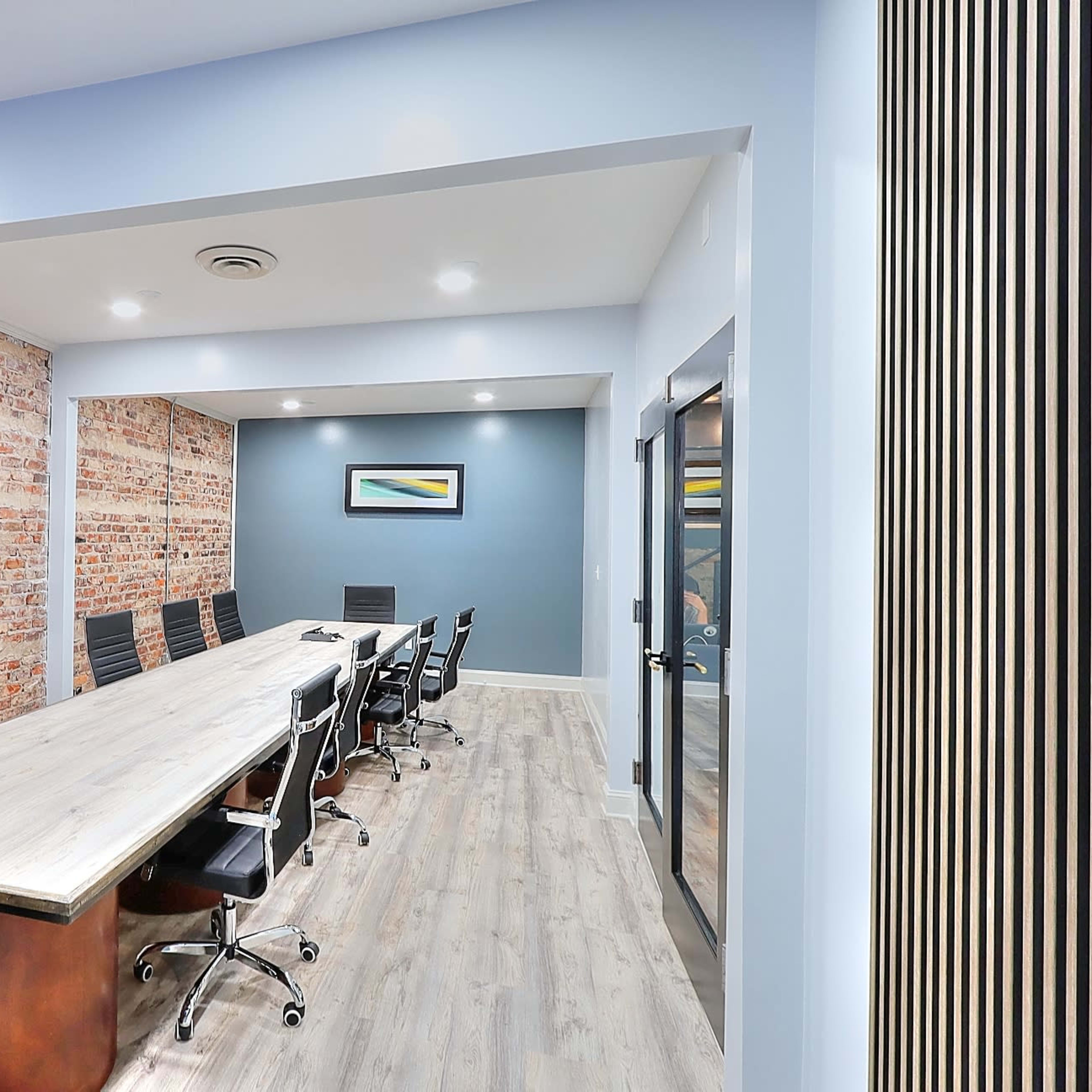 A modern conference room with a long wooden table, black chairs, and exposed brick walls.