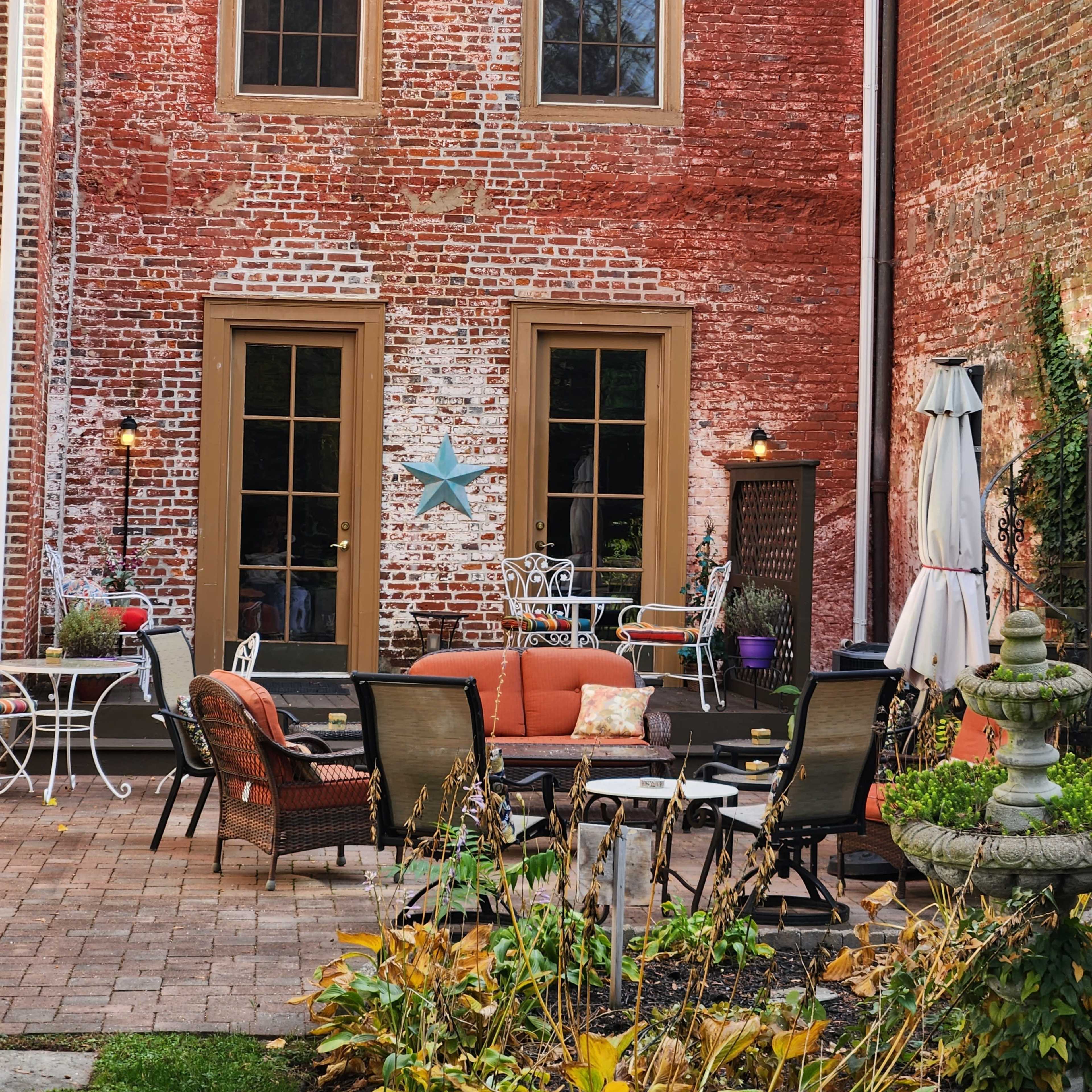 A brick-walled courtyard with outdoor seating, a star decoration, and a mix of potted plants.