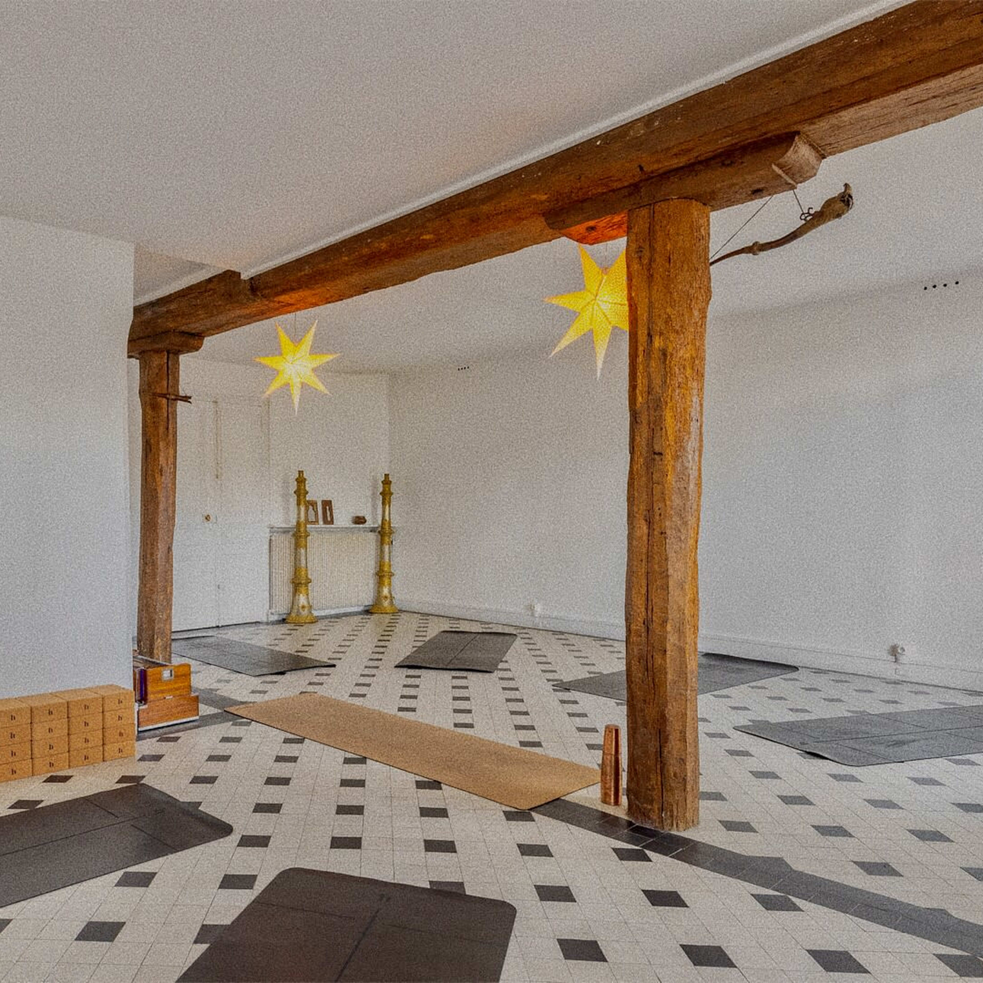 A spacious room with a patterned tiled floor, wooden beams, and a few boxes stacked on one side.