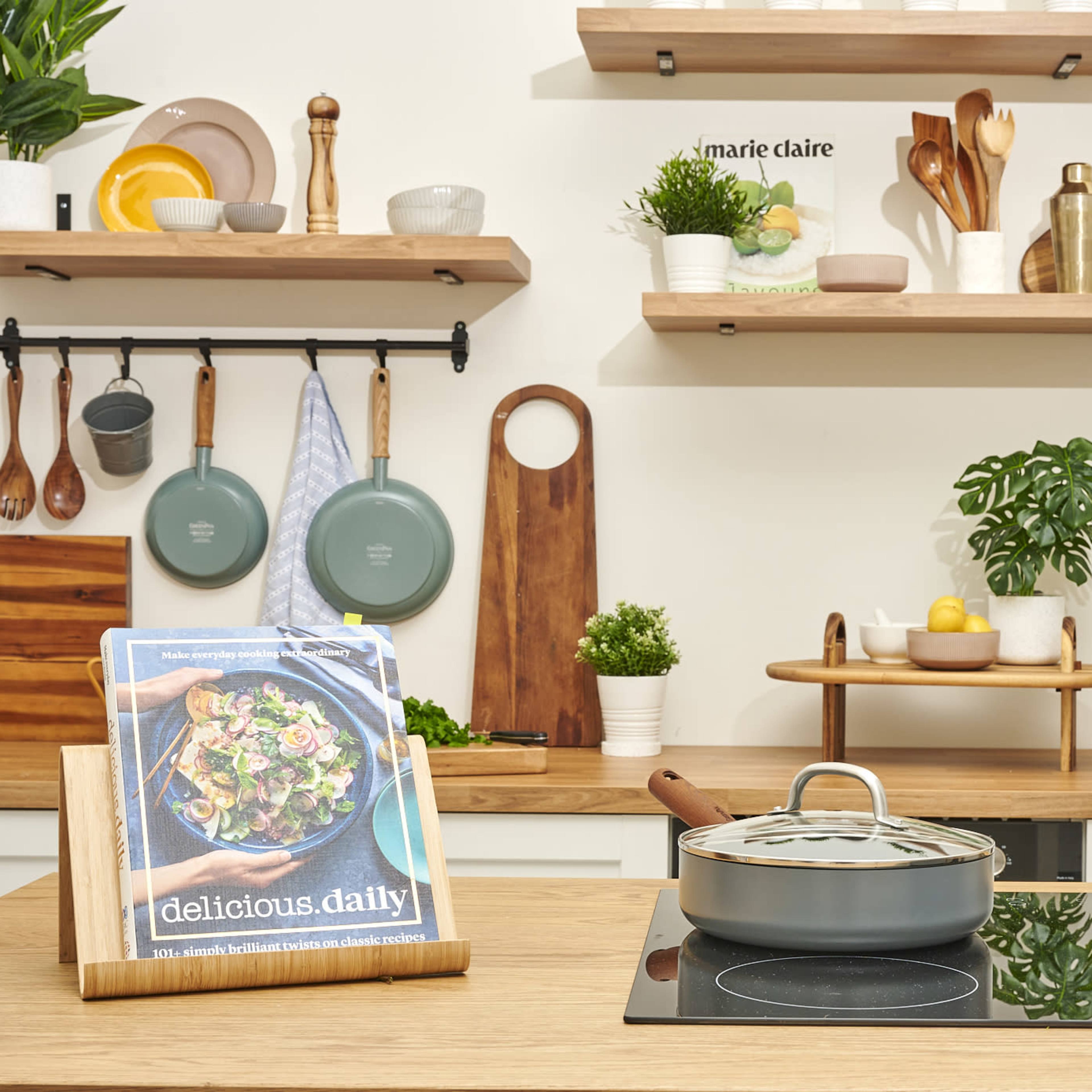 A modern kitchen features wooden shelves with various cooking utensils, pots on a stove, and a cookbook displayed on the counter.