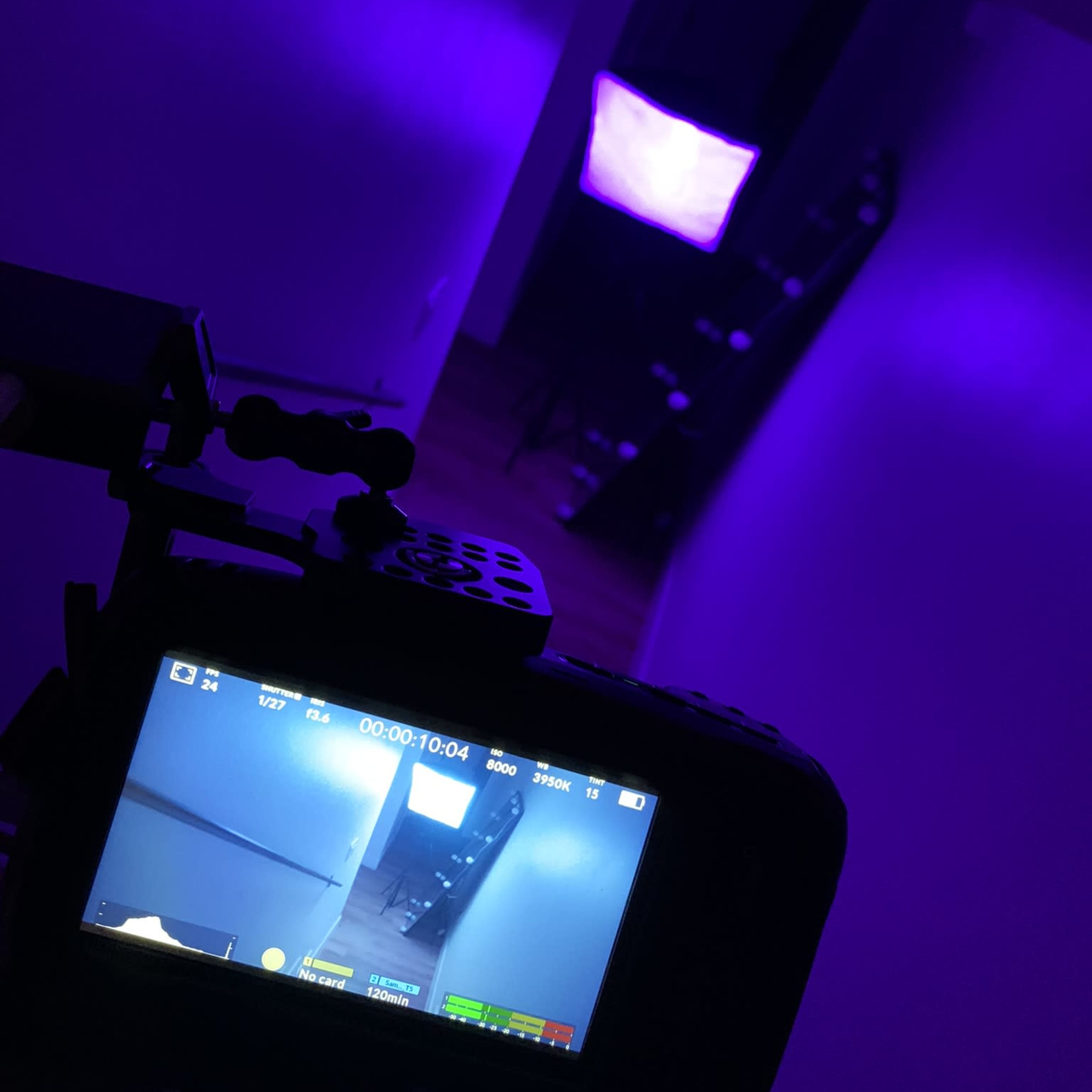 A camera is focused on a dimly lit hallway with purple lighting and a softbox in the background.