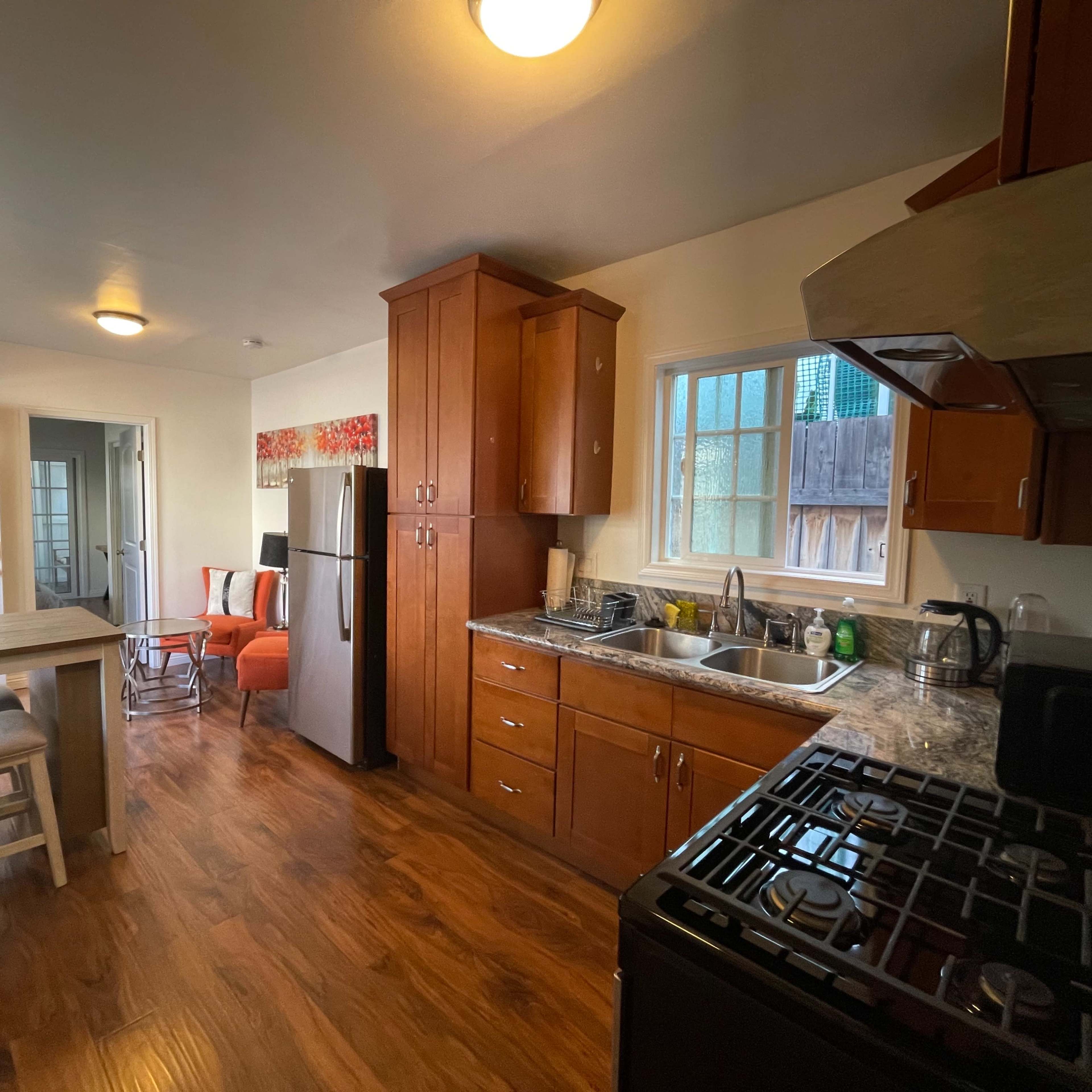 A modern kitchen features wooden cabinets, stainless steel appliances, and a small dining area with a table and chairs.