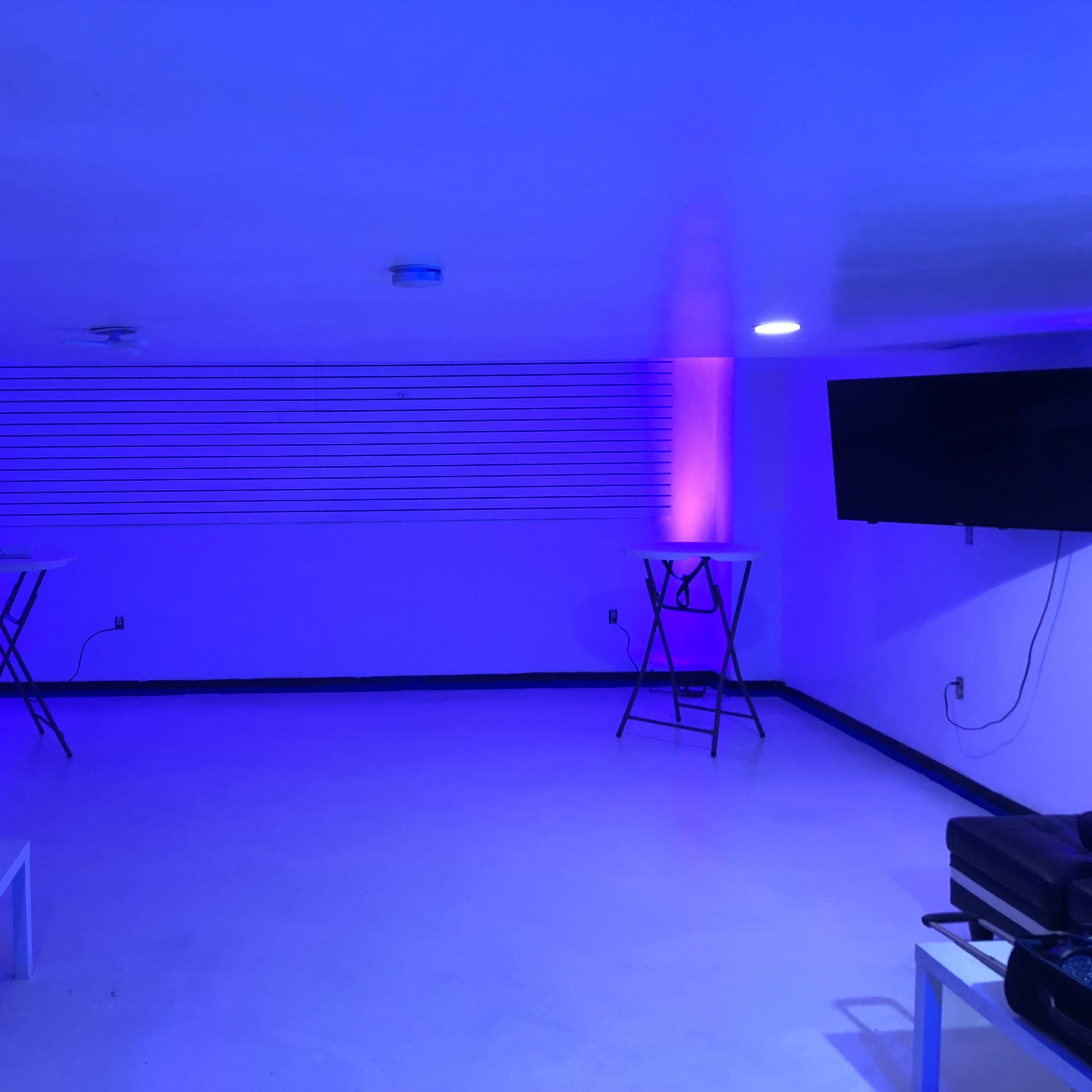 A room with a white floor, two televisions mounted on the walls, and blue lights illuminating the space.
