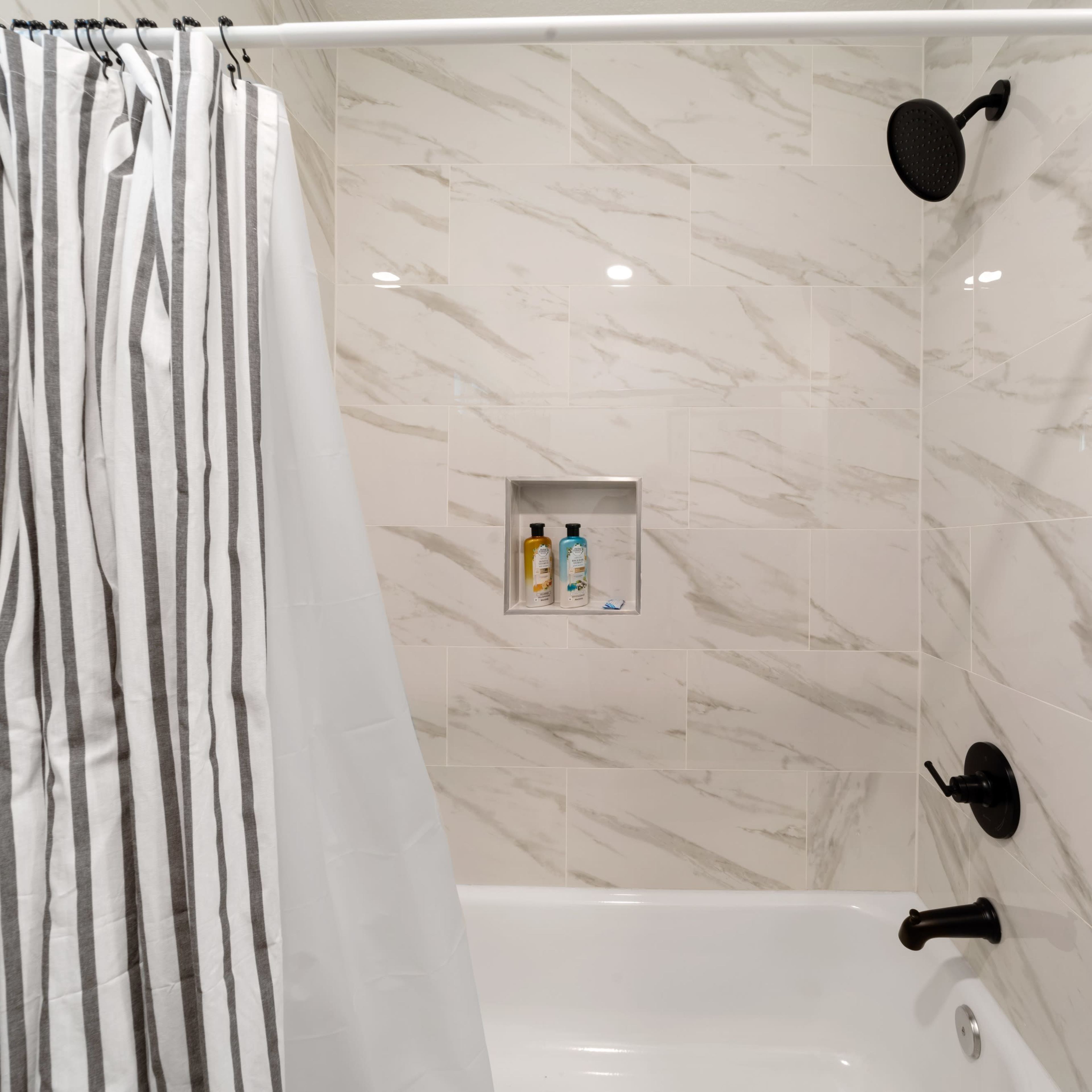 A shower area with a striped curtain, tiled walls, and a built-in shelf containing toiletries.