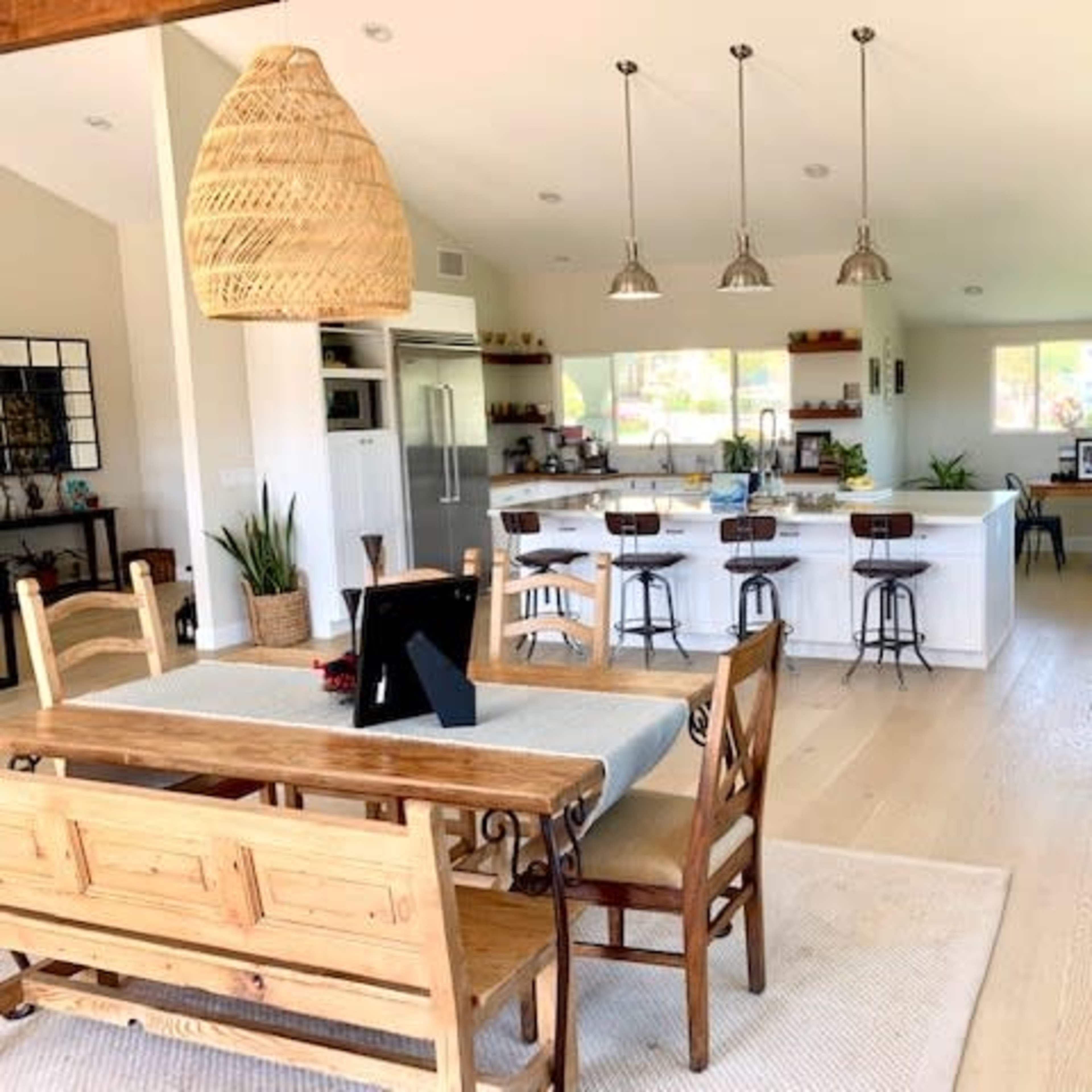 A spacious open-concept kitchen and dining area features a large wooden table, bar stools at an island, and pendant lighting.