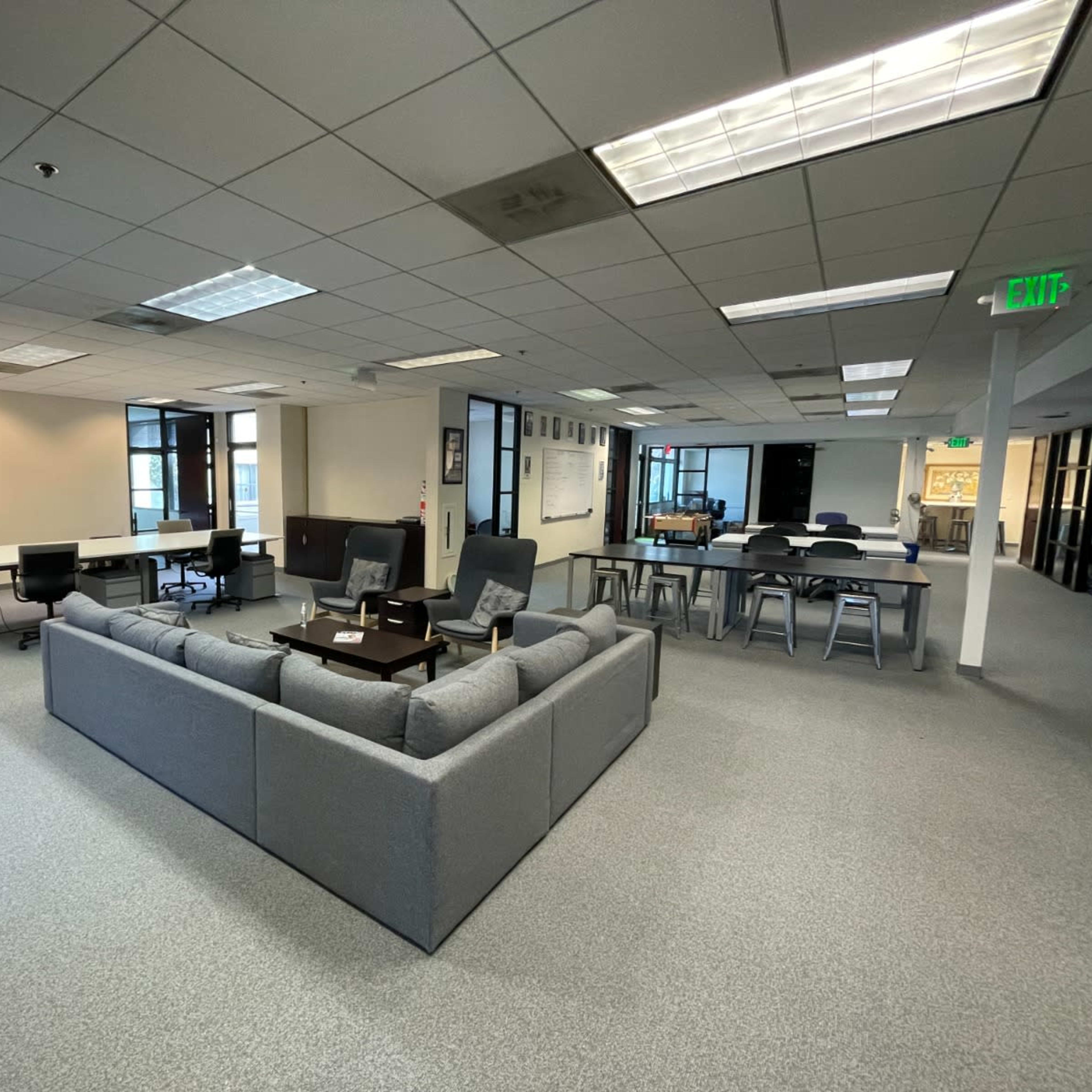 A spacious office area with a gray sectional couch in the center, surrounded by tables and chairs.