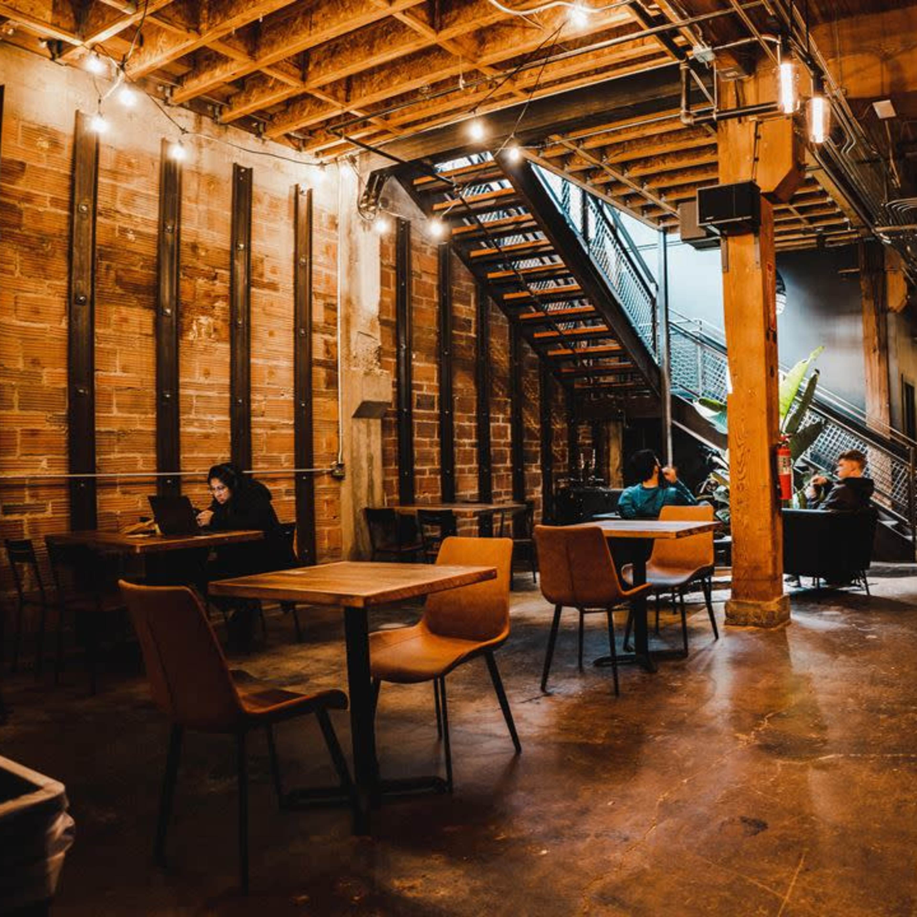 A modern café featuring wooden walls, a staircase in the background, and patrons seated at tables.