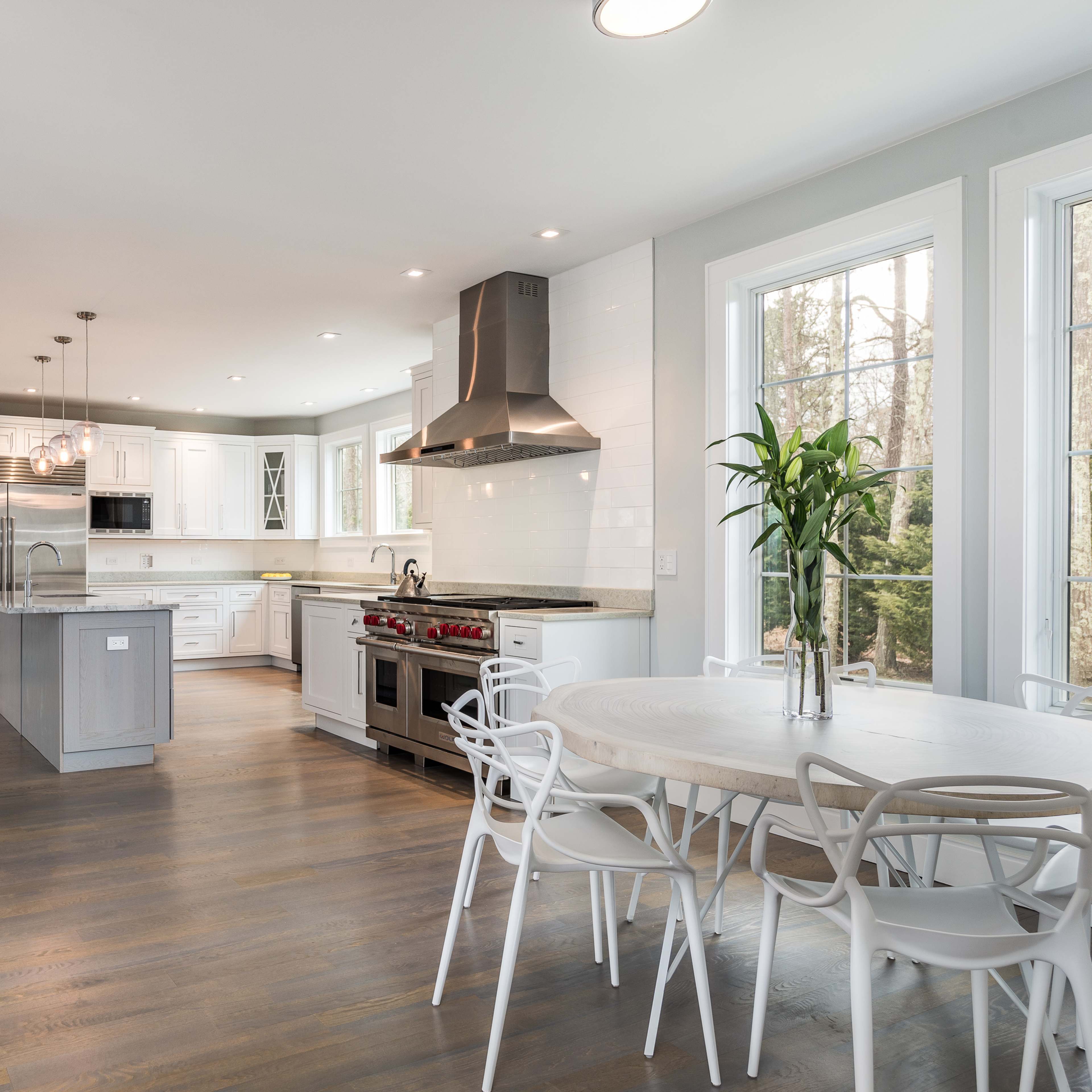 A modern kitchen with a central island, stainless steel appliances, and a round dining table surrounded by white chairs.
