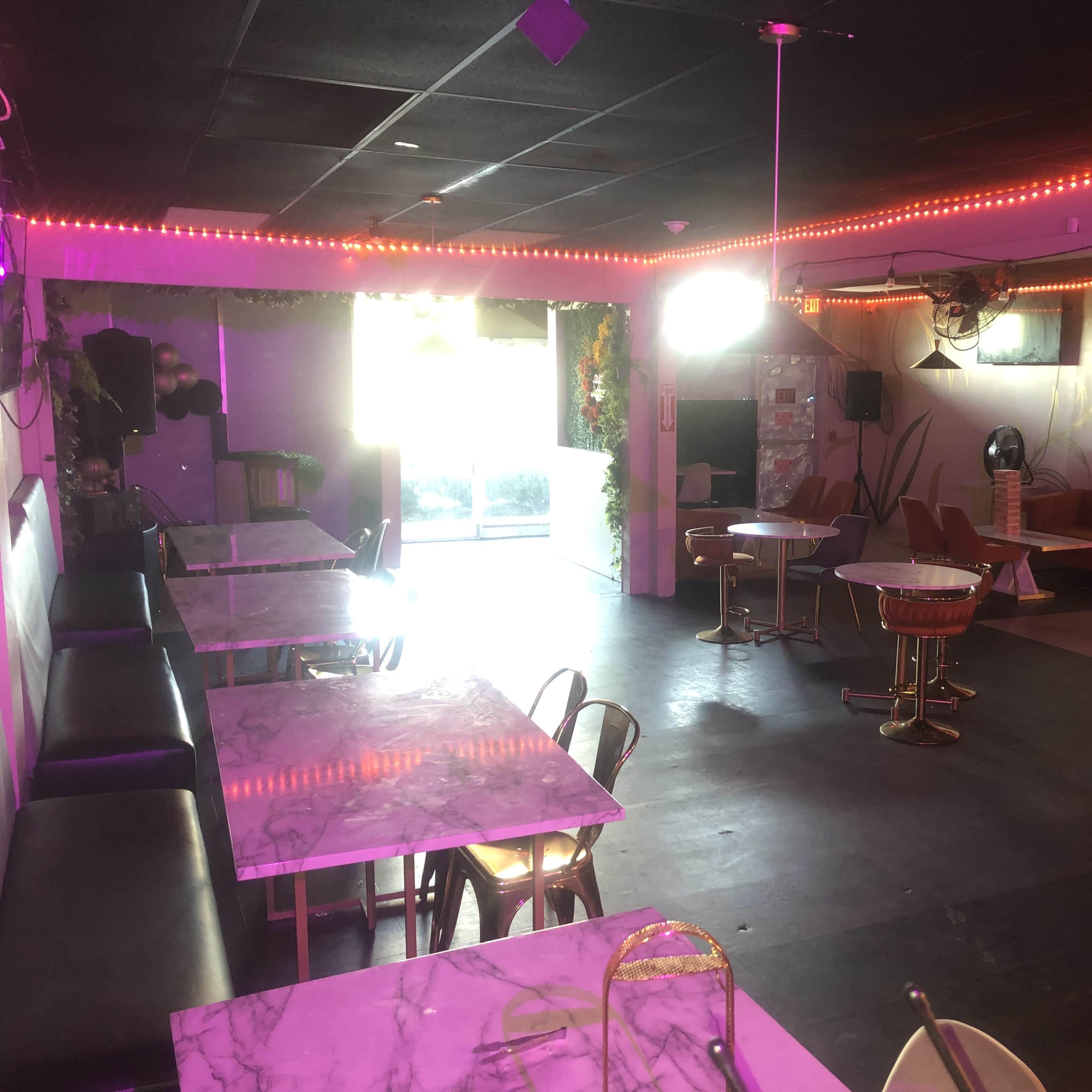 An interior of a venue with marble-topped tables, pink lighting, and a mix of seating arrangements.