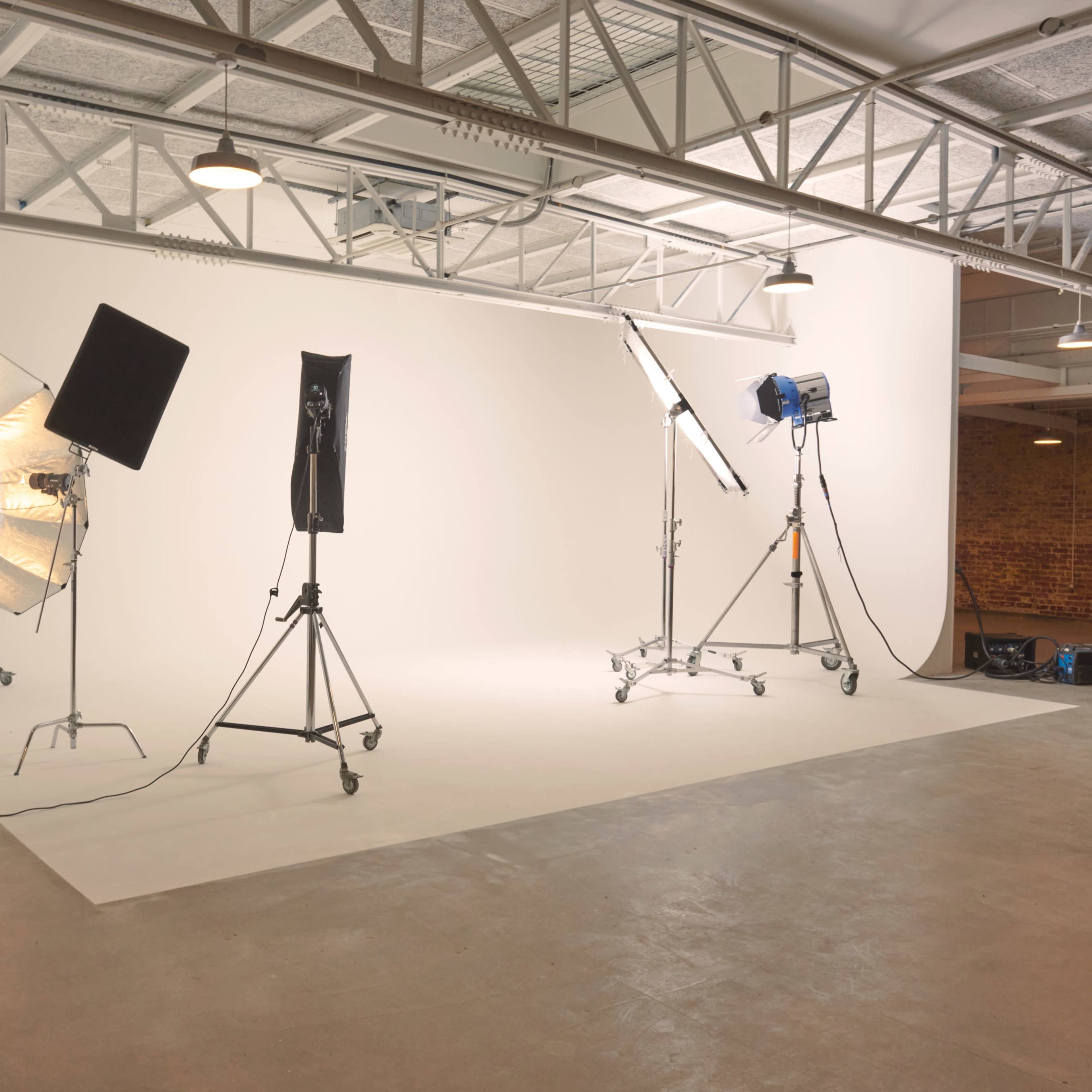 A photography studio with various lighting equipment set up against a plain white backdrop.