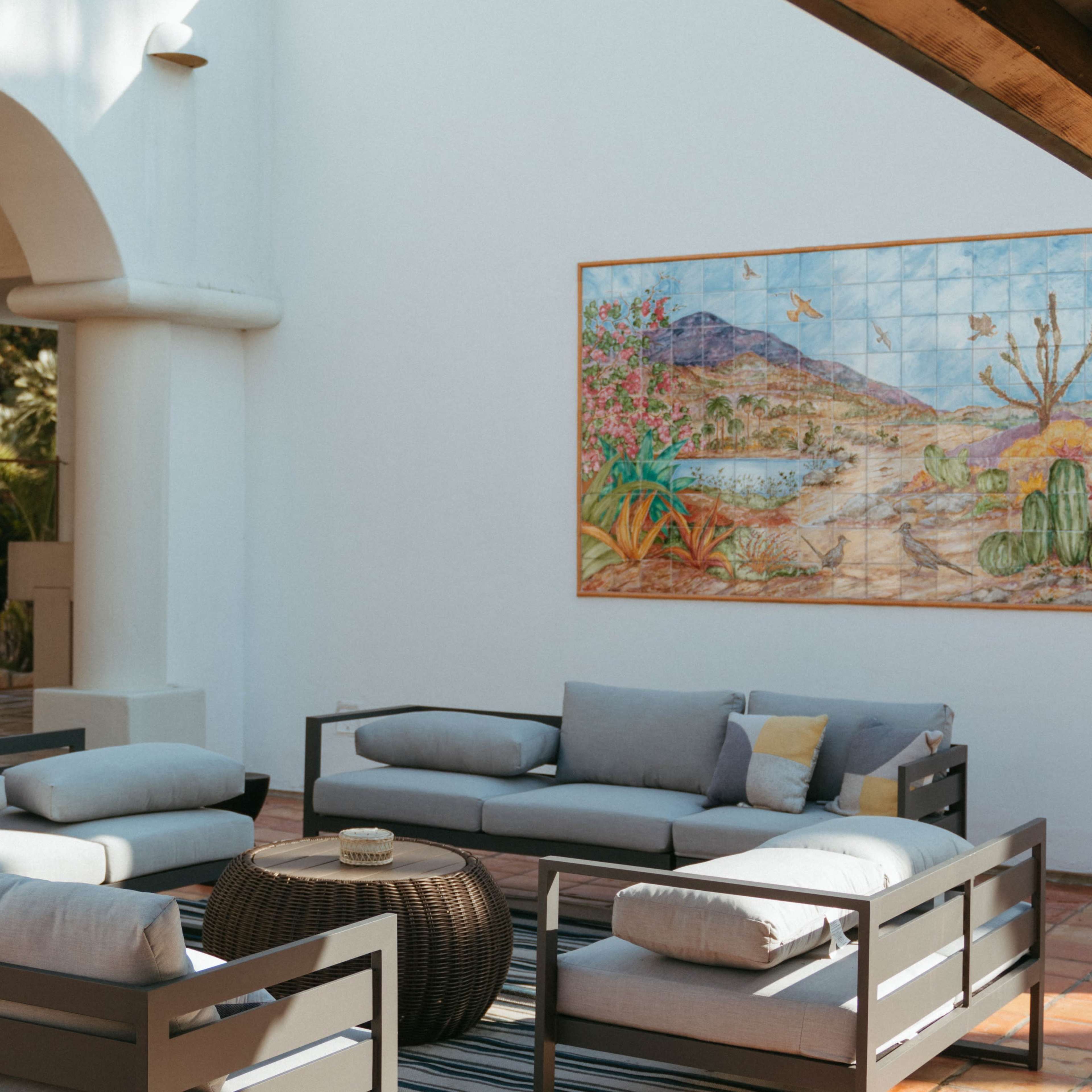 A seating area styled with gray sofas and a round coffee table, set against a backdrop of a colorful mural depicting a desert landscape.