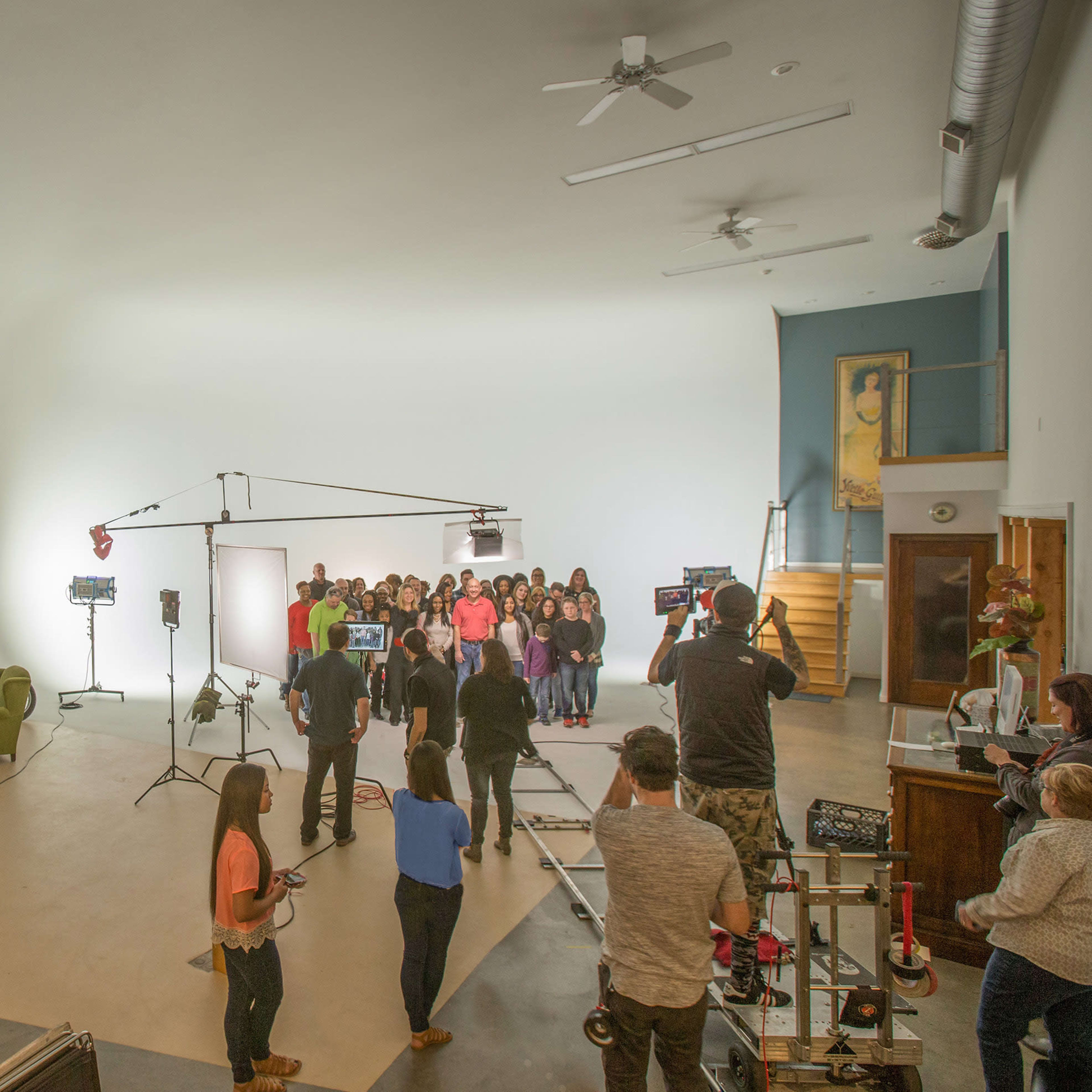 A group of people stands in a well-lit studio surrounded by filming equipment and lighting setups.