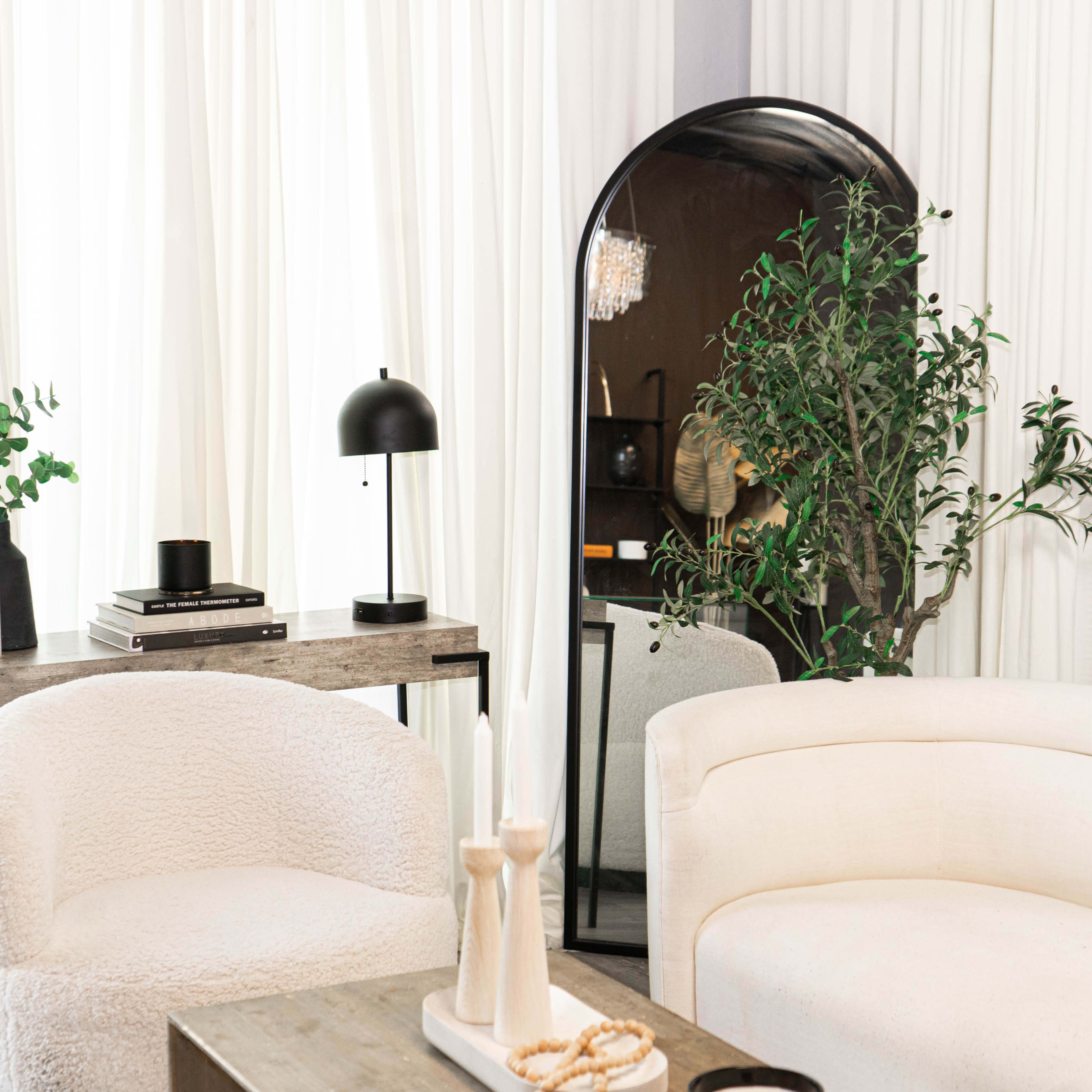 A modern living space featuring a curved white sofa, a small side table with a lamp, and a large mirror reflecting a plant and decorative items.