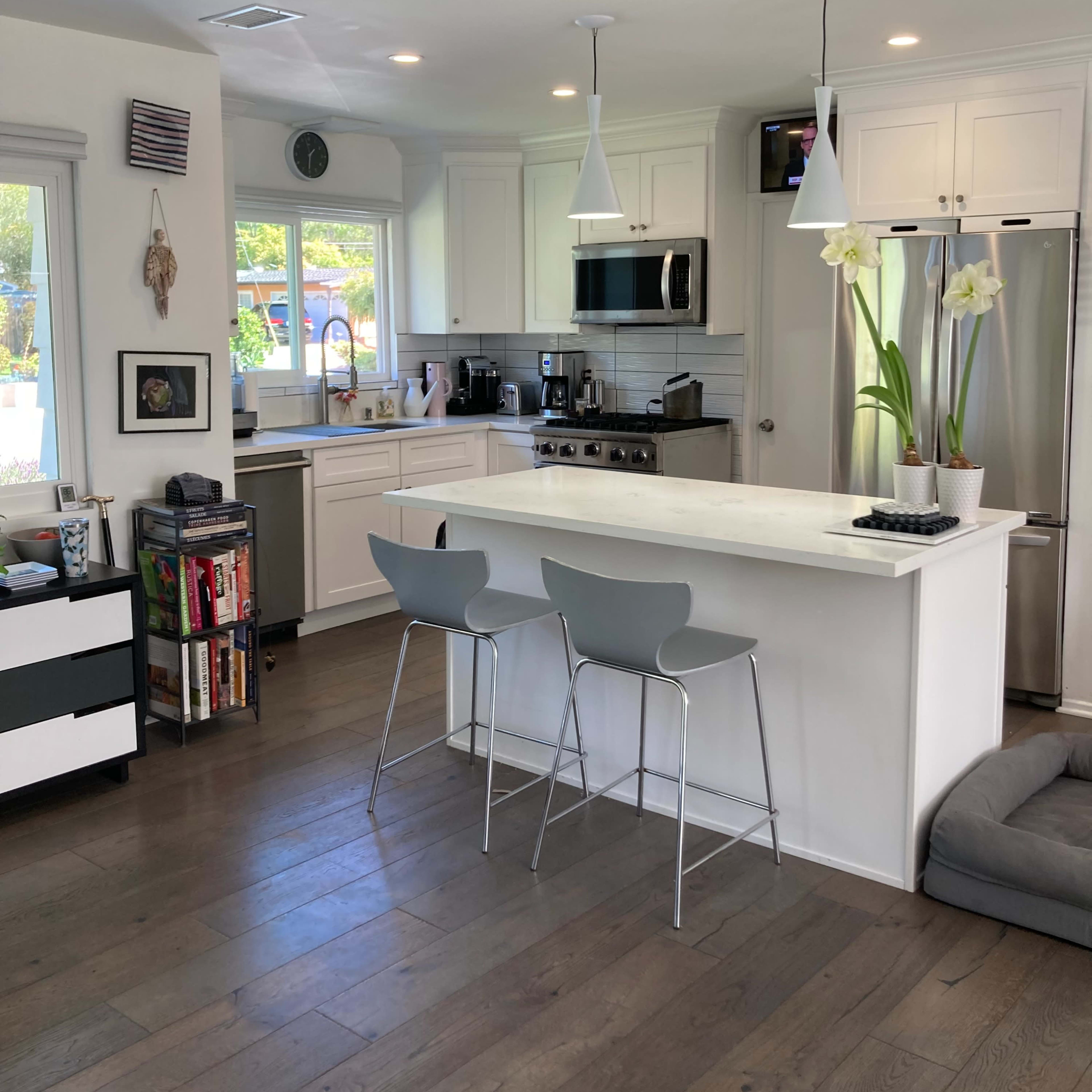 A modern kitchen features white cabinetry, a marble countertop island with two gray stools, and stainless steel appliances.