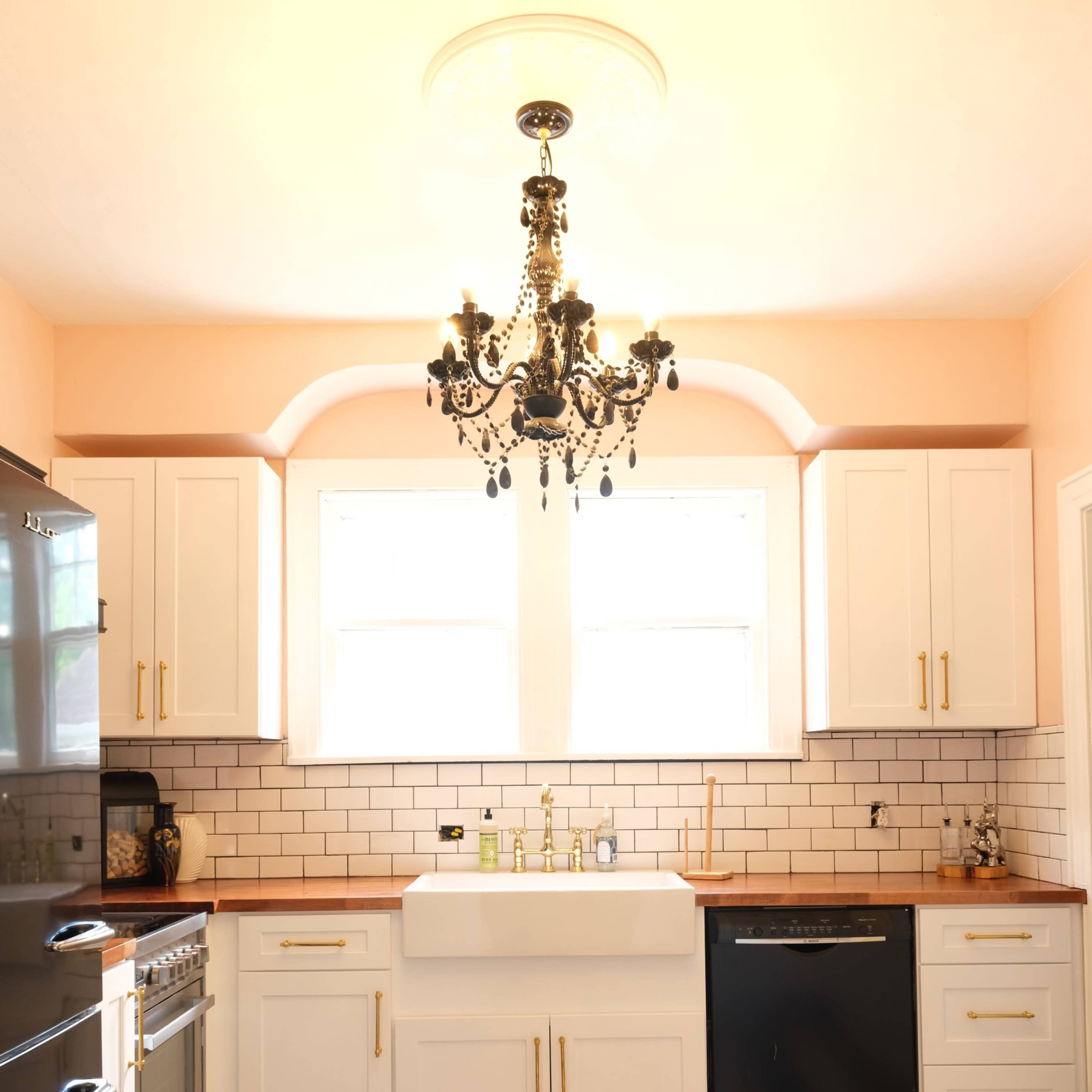 A kitchen featuring a white farmhouse sink, black and white checkered floor, and a chandelier above a central island.