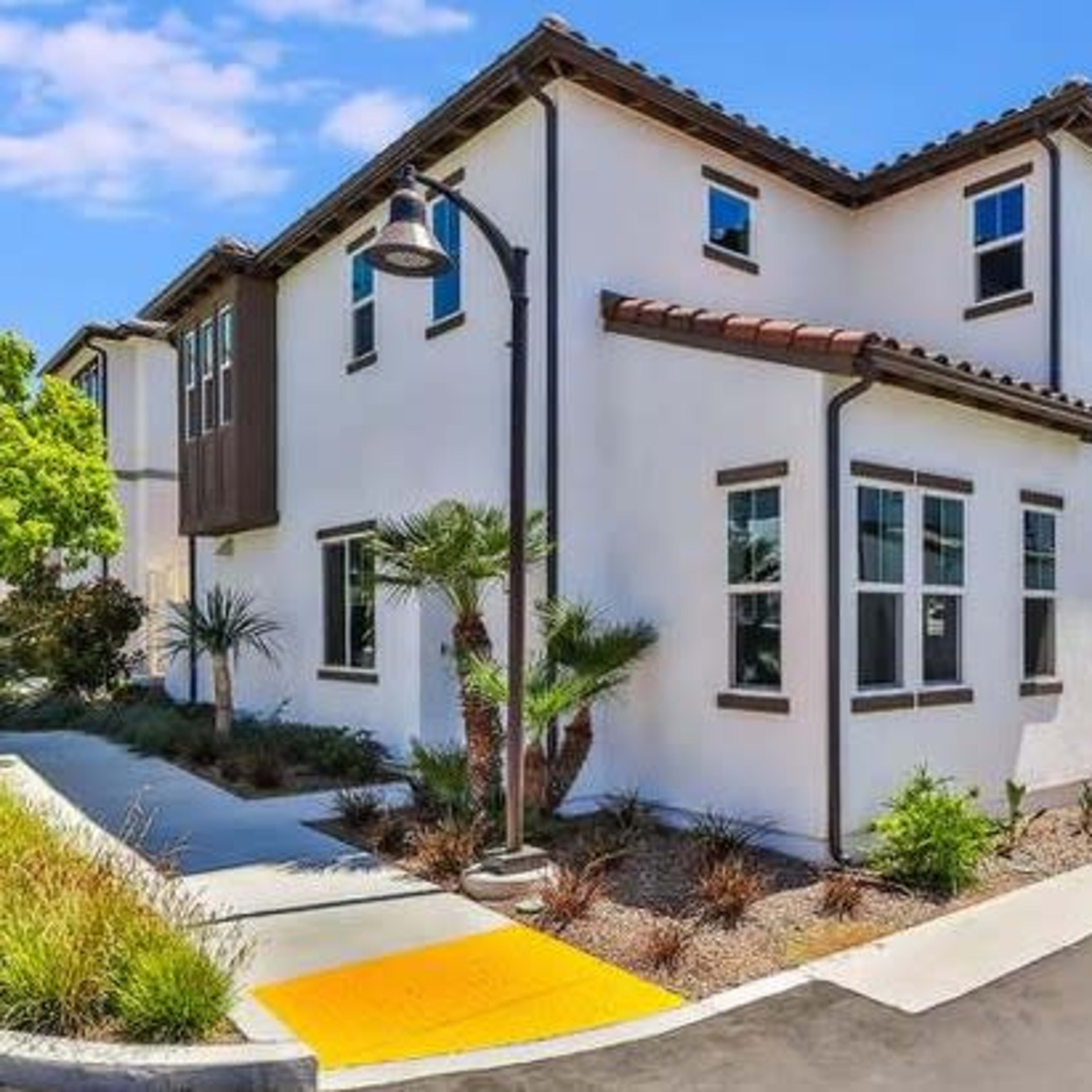 A modern two-story house with white walls, a tiled roof, and landscaping along a walkway and driveway.