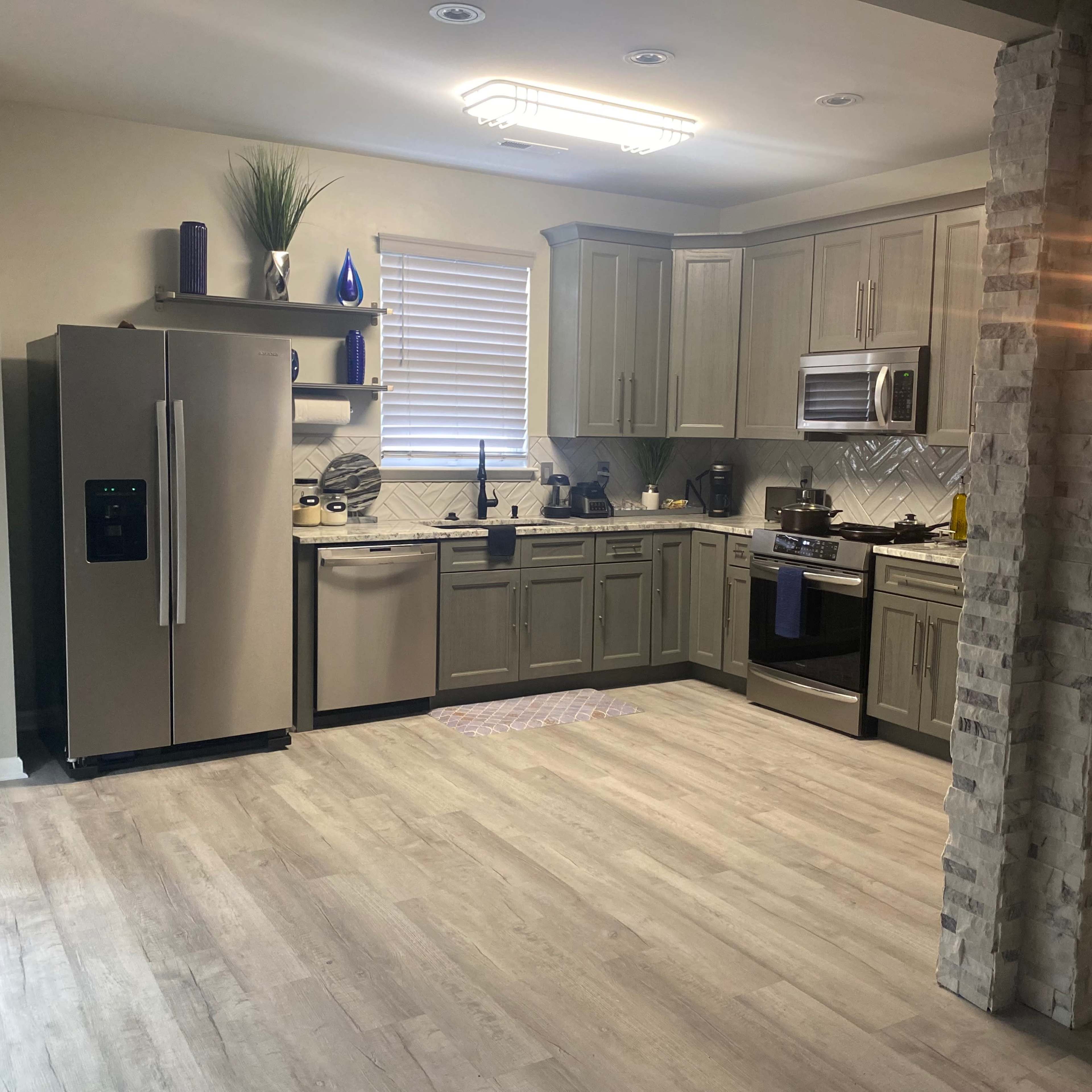 A modern kitchen with gray cabinets, stainless steel appliances, and a combination of tiled and wooden flooring.