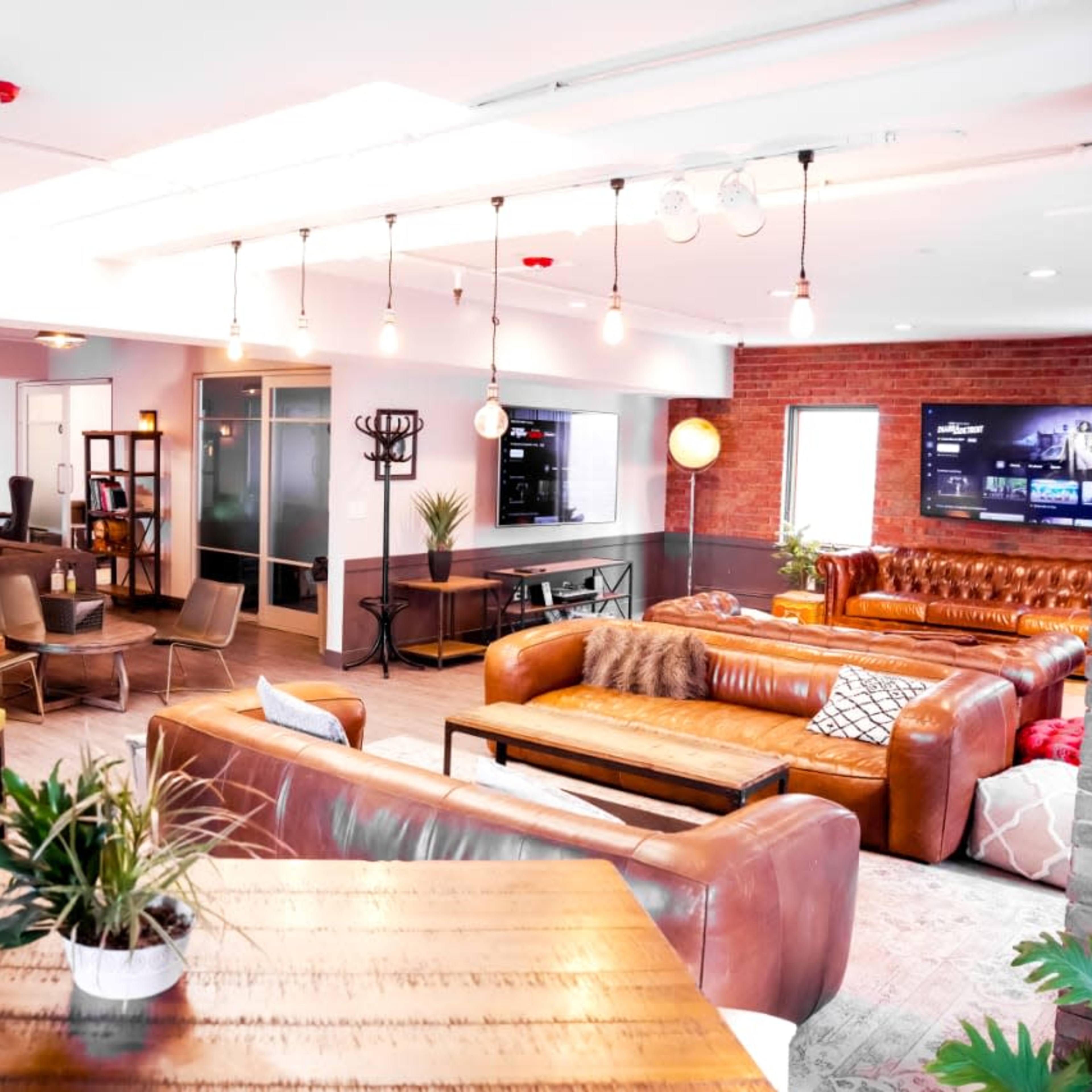 A modern, open office space with various seating areas, wooden tables, and a mix of leather sofas and chairs.