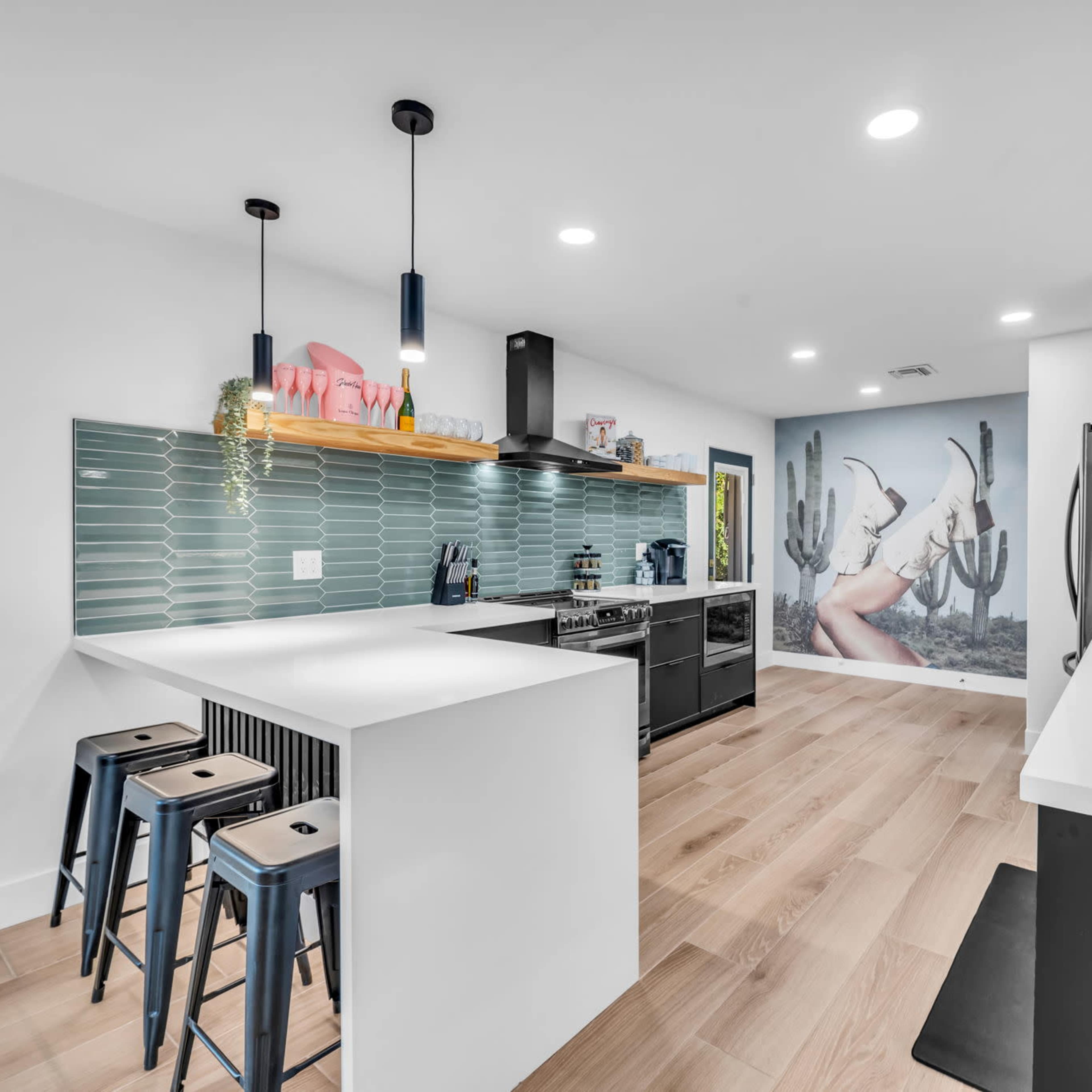 A modern kitchen with a sleek design featuring a central island, bar stools, and a mural of a woman among cacti on the wall.