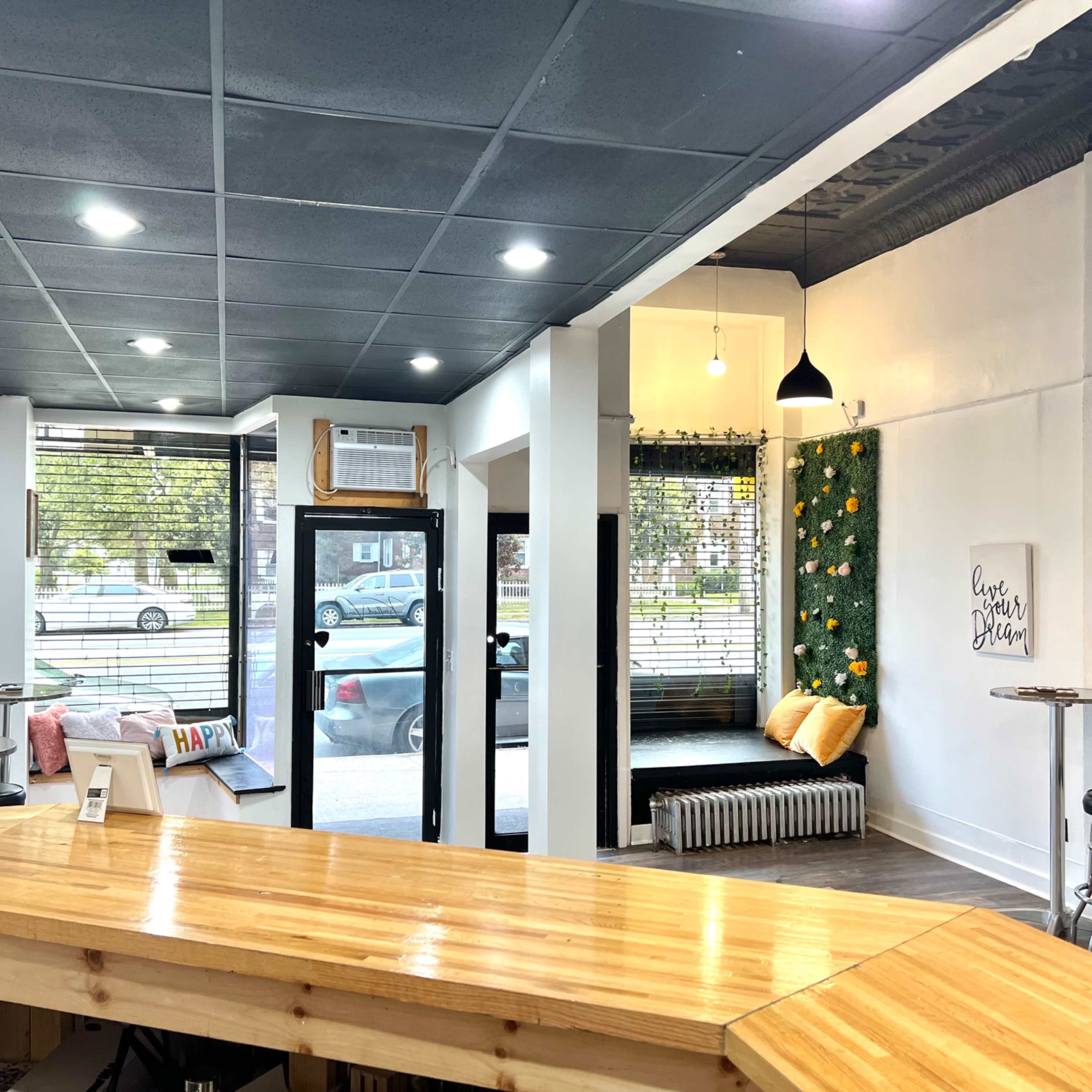 A modern coffee shop interior with a wooden counter, seating area with plants on the wall, and large windows providing natural light.