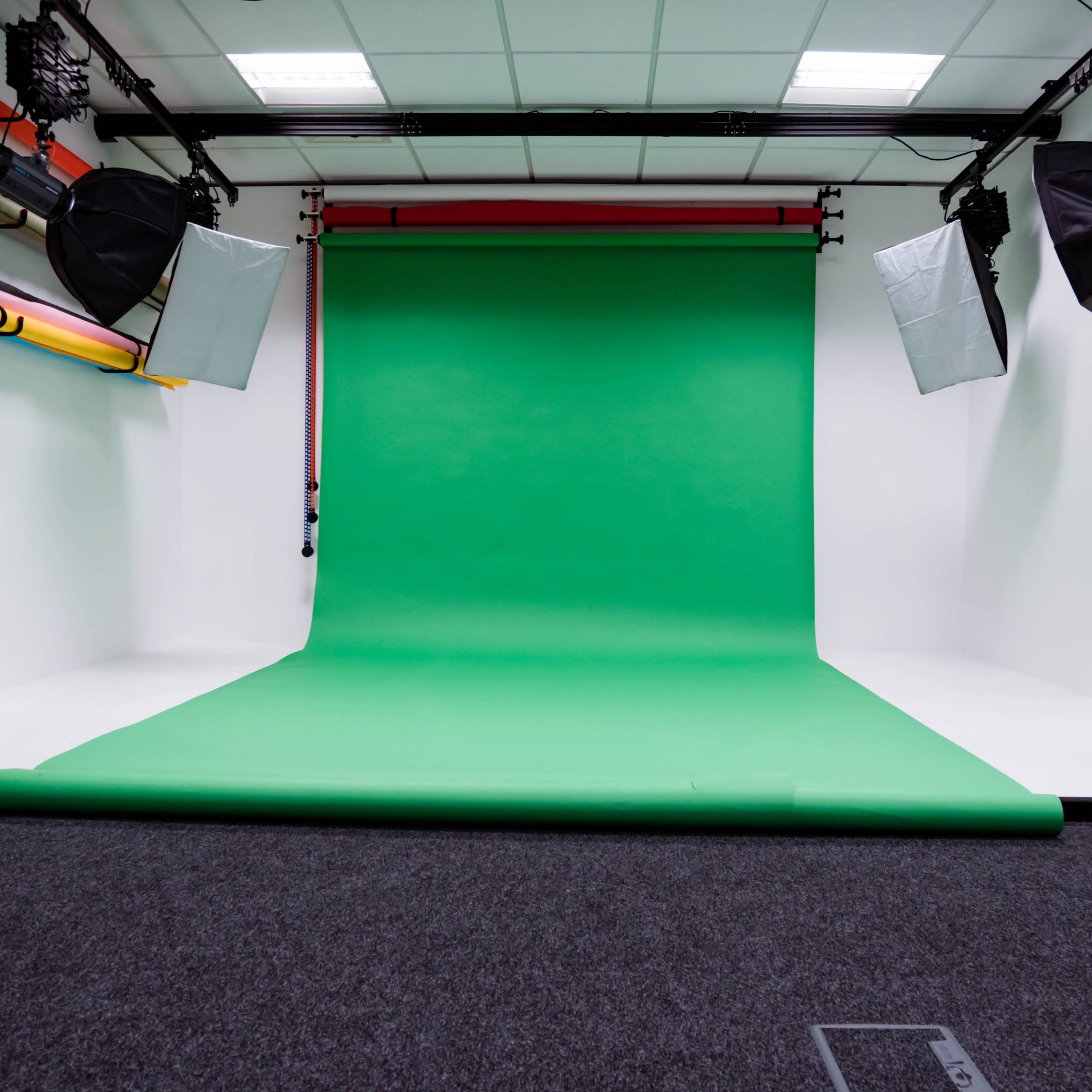A photography studio featuring a green backdrop, studio lighting, and a dark carpeted floor.