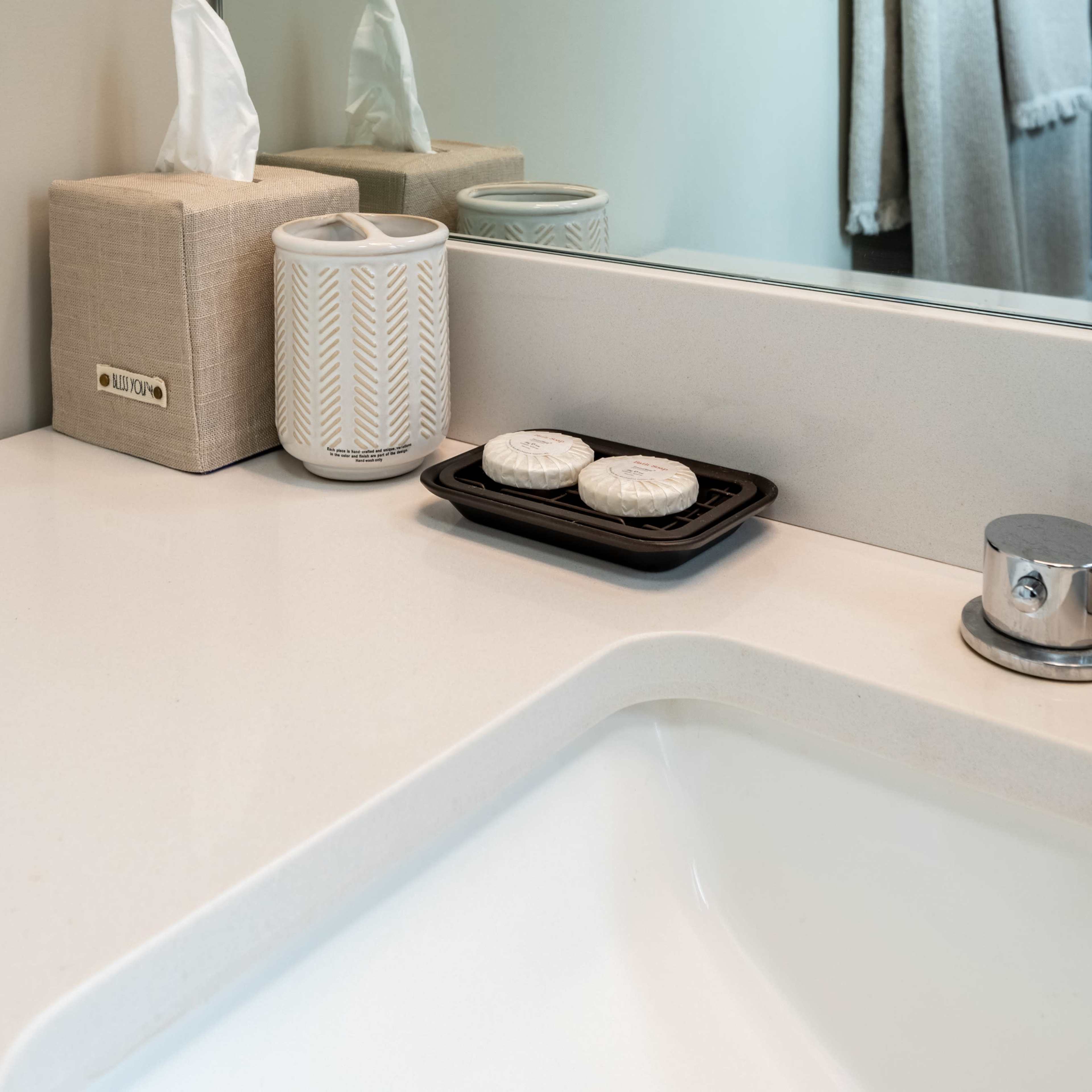 A bathroom countertop features a tissue box, a decorative container, and a plate with two soap bars near a sink.