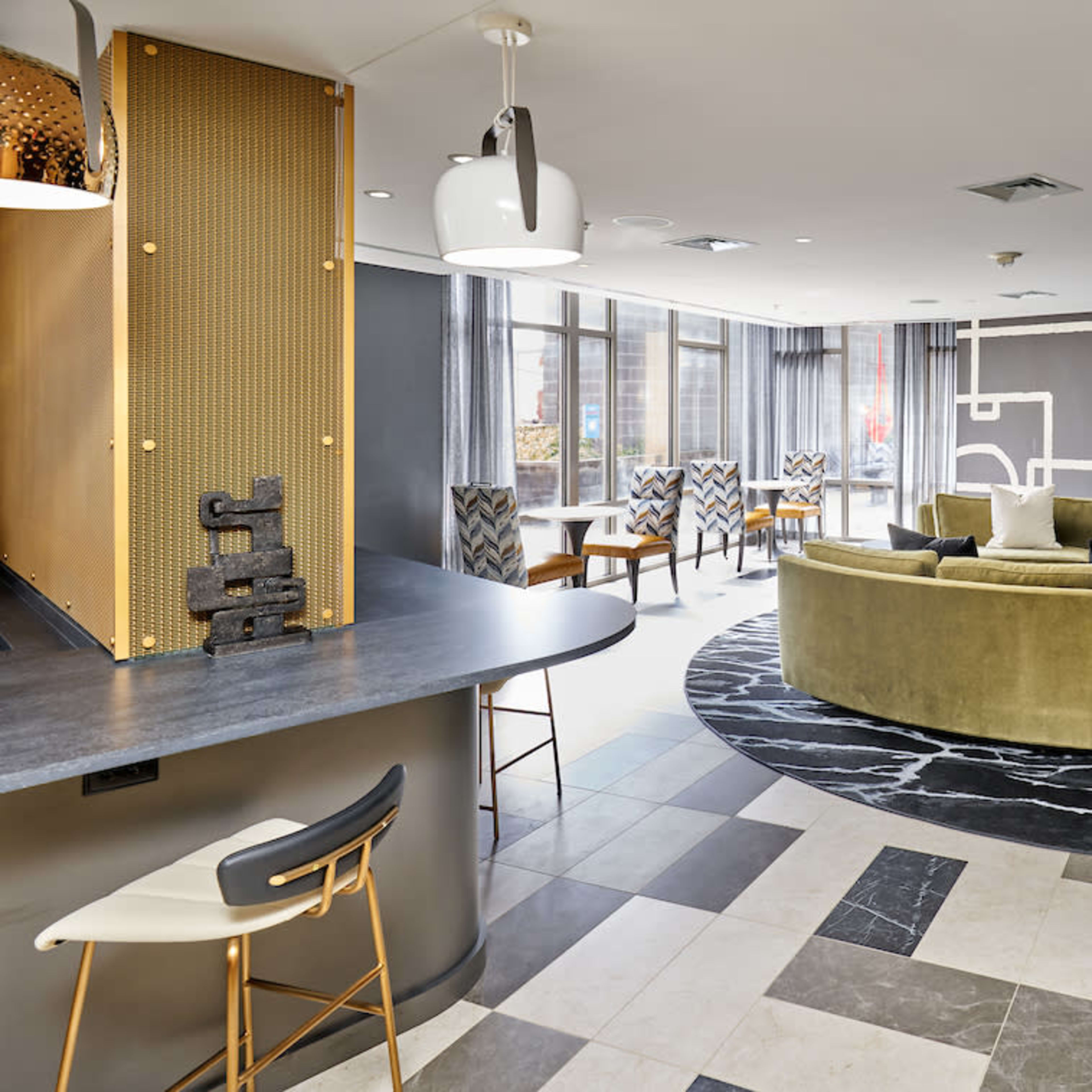 A modern lounge area featuring a curved green sofa, a patterned rug, and a bar with high chairs.