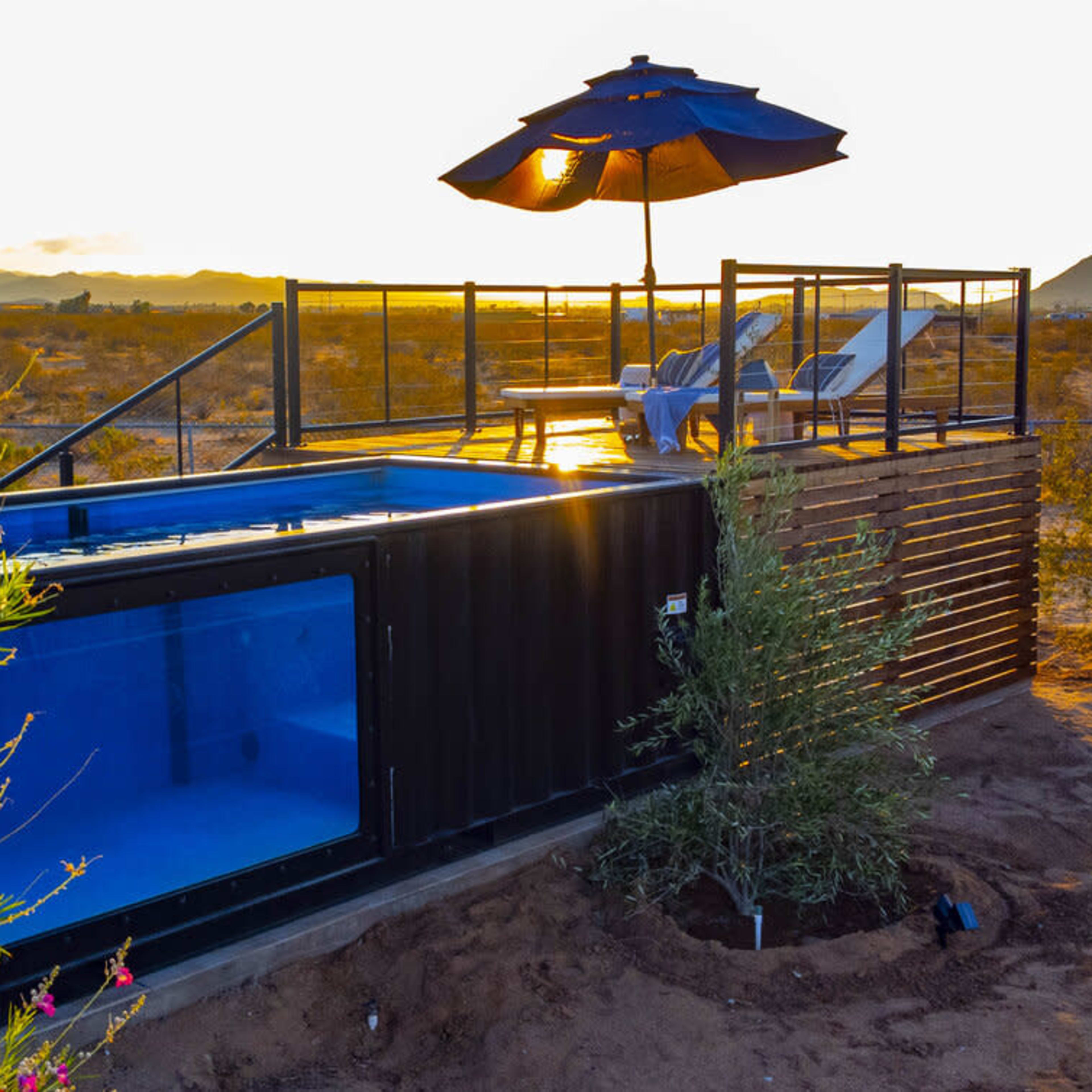 A shipping container is transformed into a modern living space with a pool and a deck, set against a desert landscape at sunset.