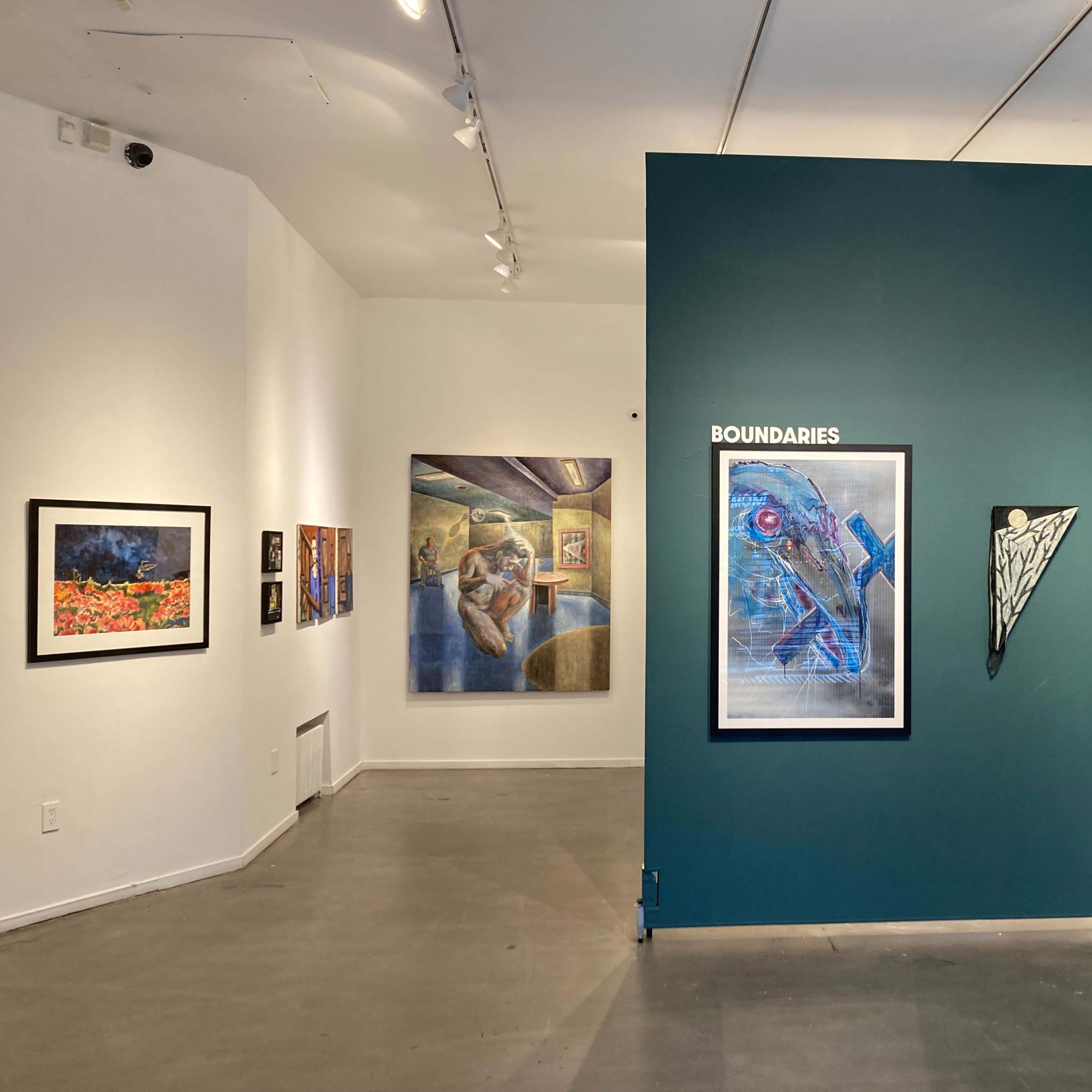 An art gallery featuring framed artworks on white walls and a green accent wall displaying various pieces, including a work titled "Boundaries."